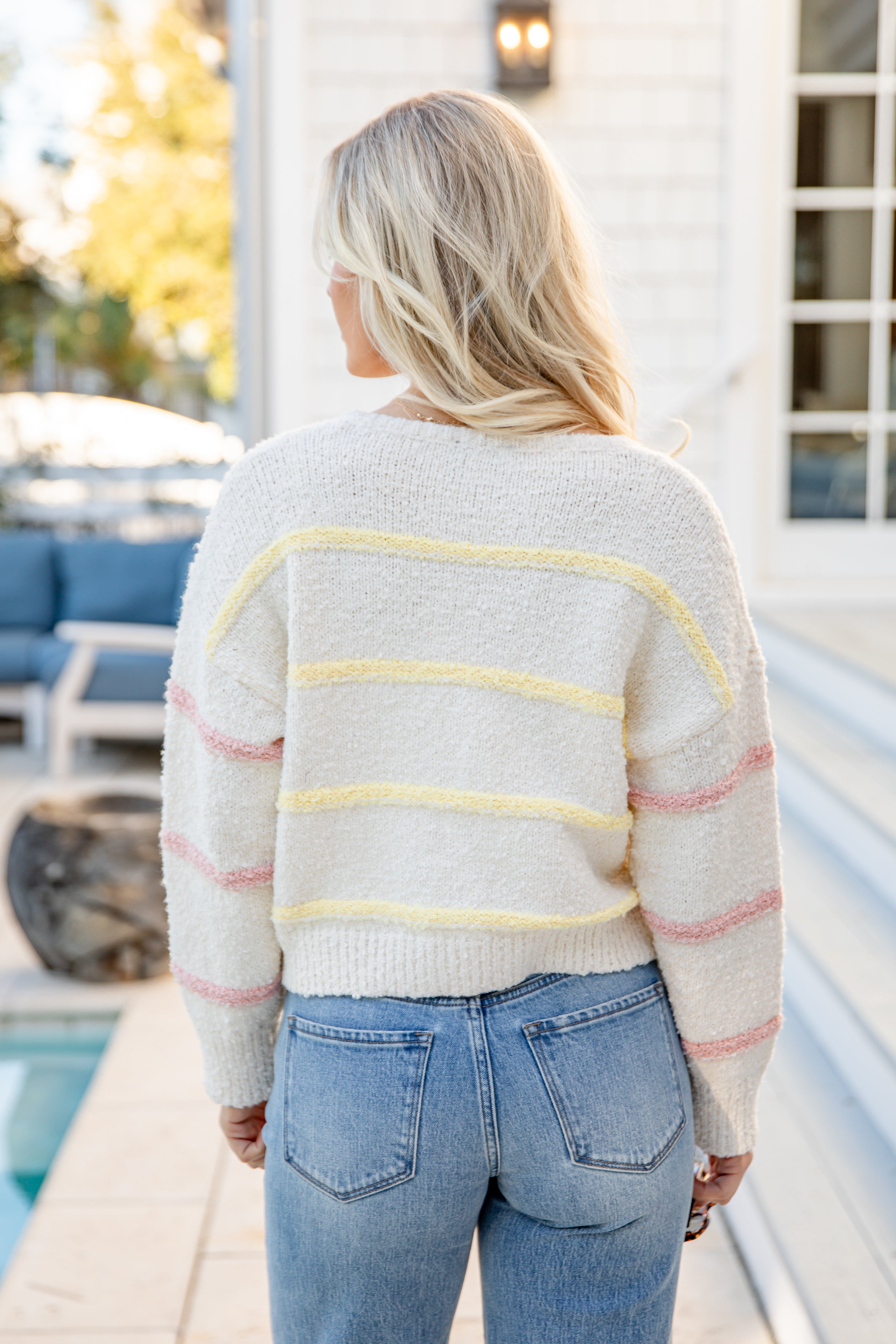 Person wearing a striped sweater and jeans standing by a poolside.
