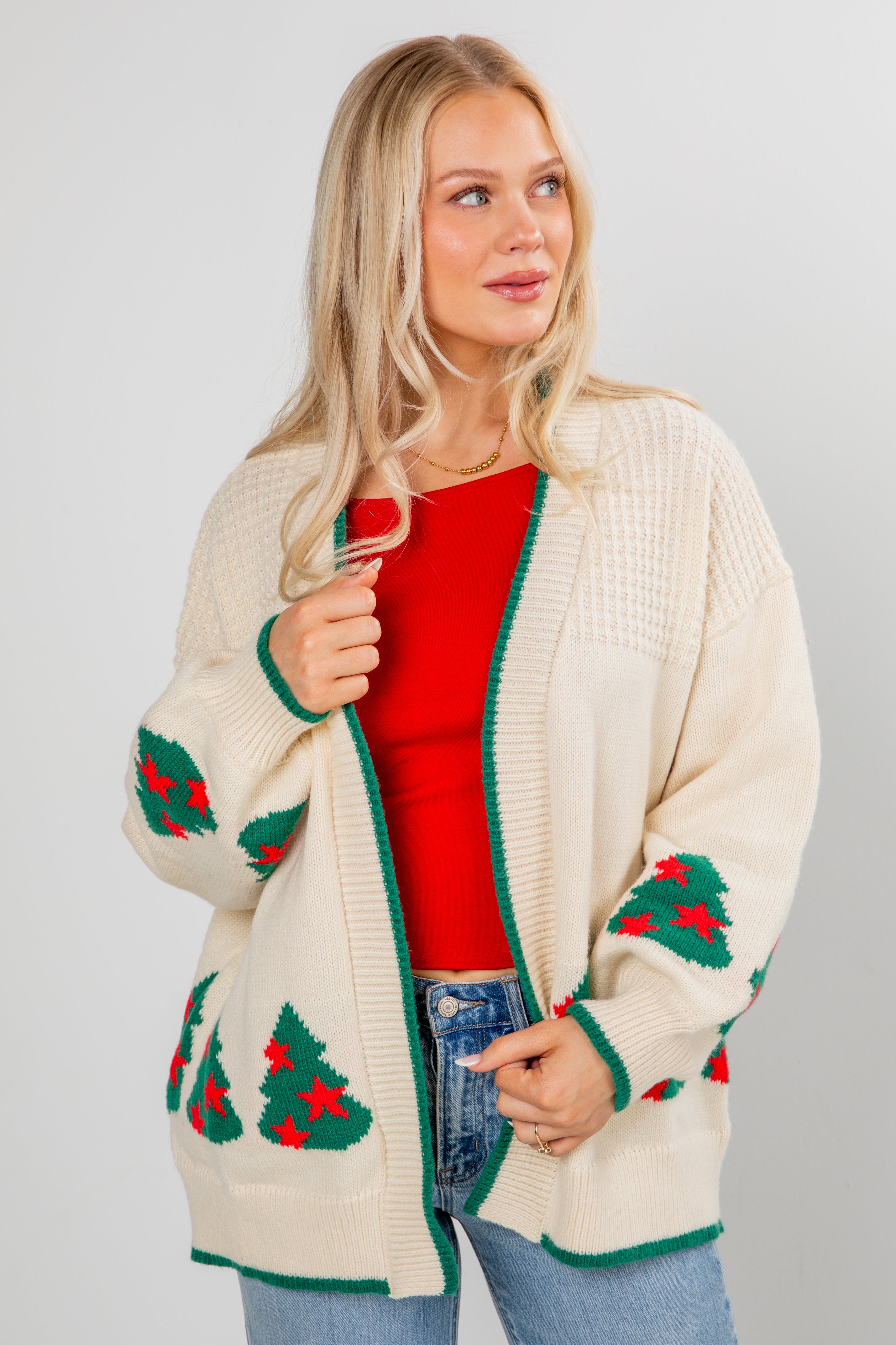 Woman wearing a cream cardigan with Christmas tree patterns on a plain background