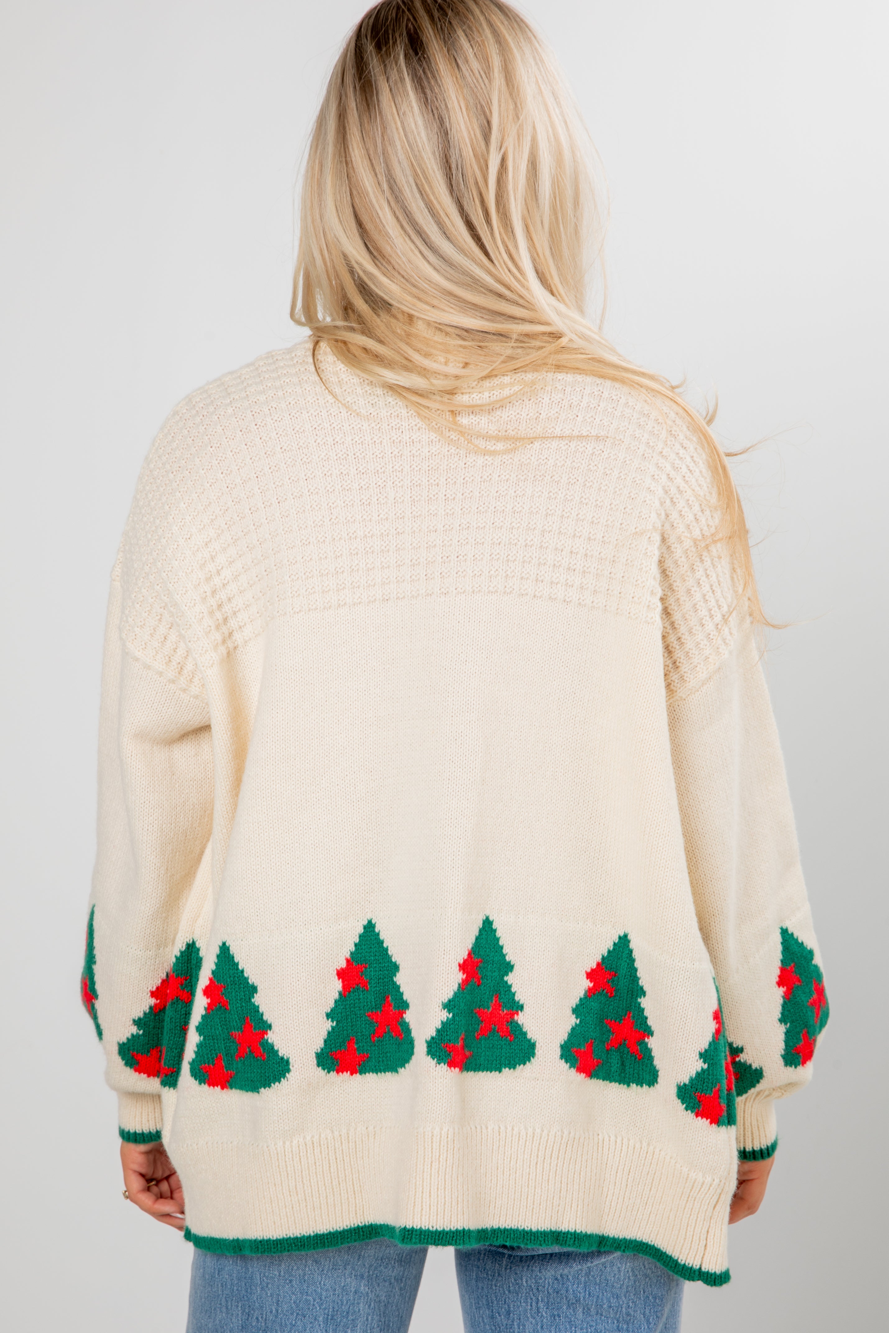 Person wearing a cream sweater with Christmas tree patterns on a plain background