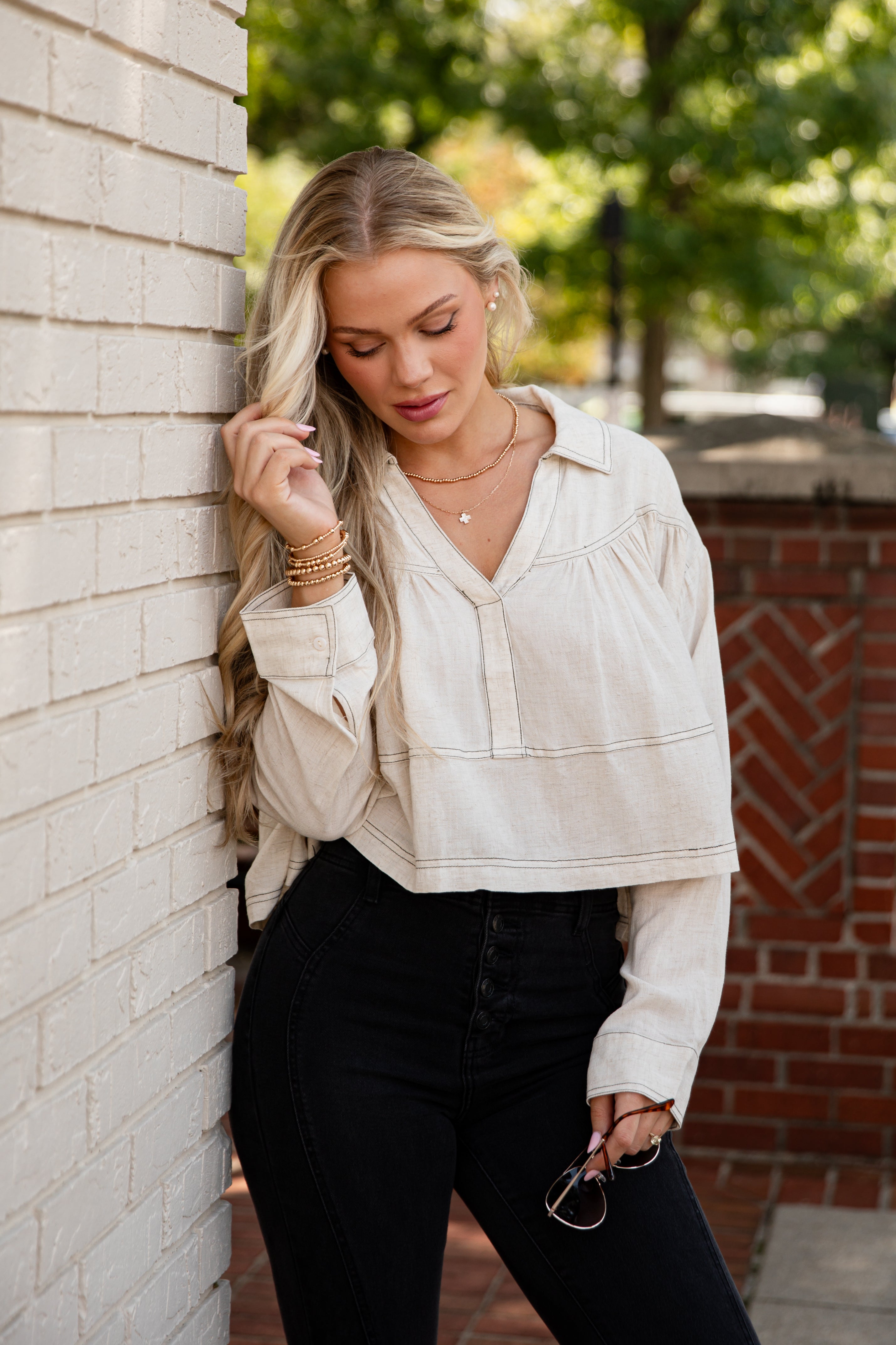 Woman in a white blouse and black pants leaning against a brick wall.