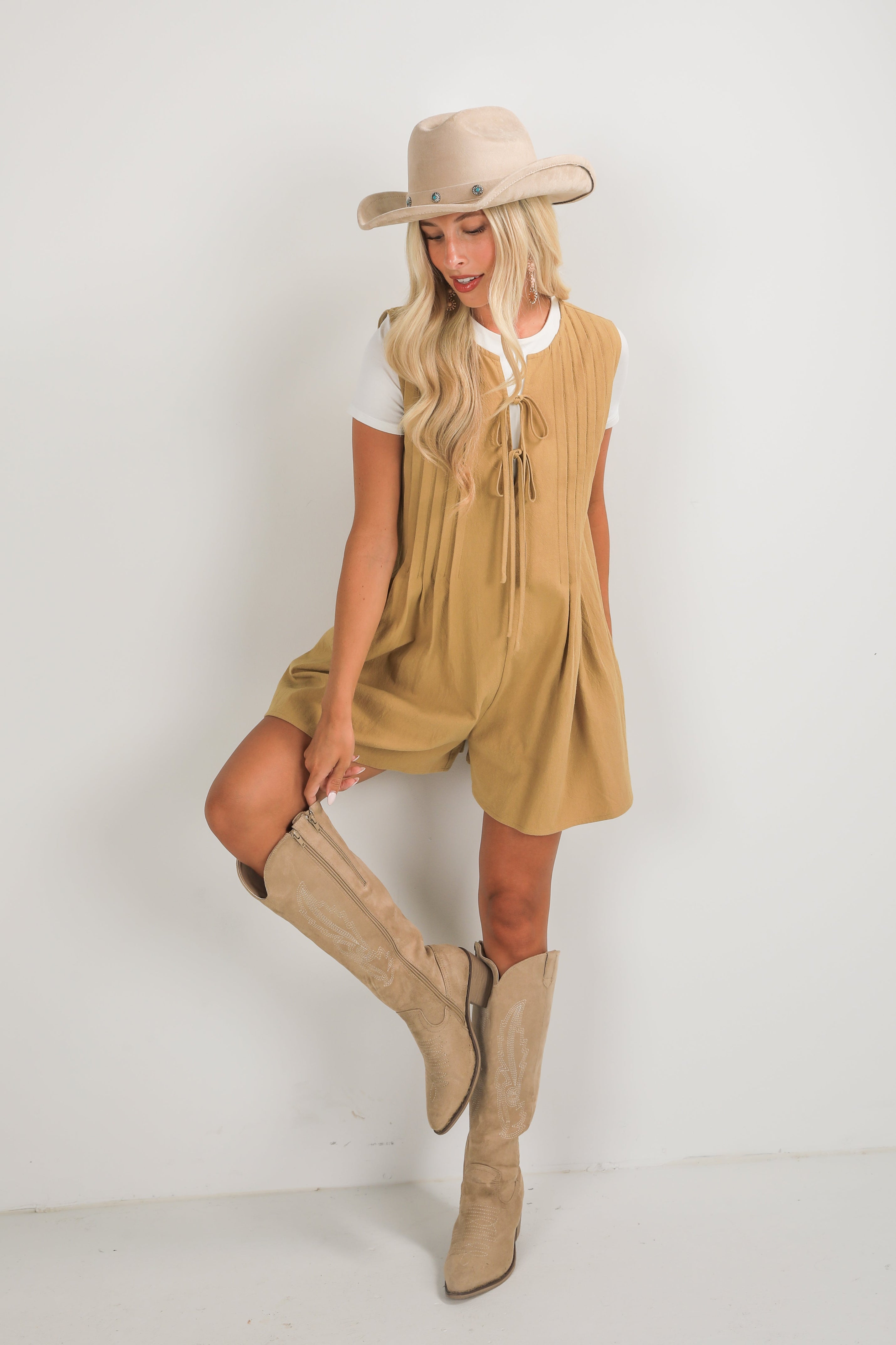 Woman wearing a beige dress, boots, and hat on a white background