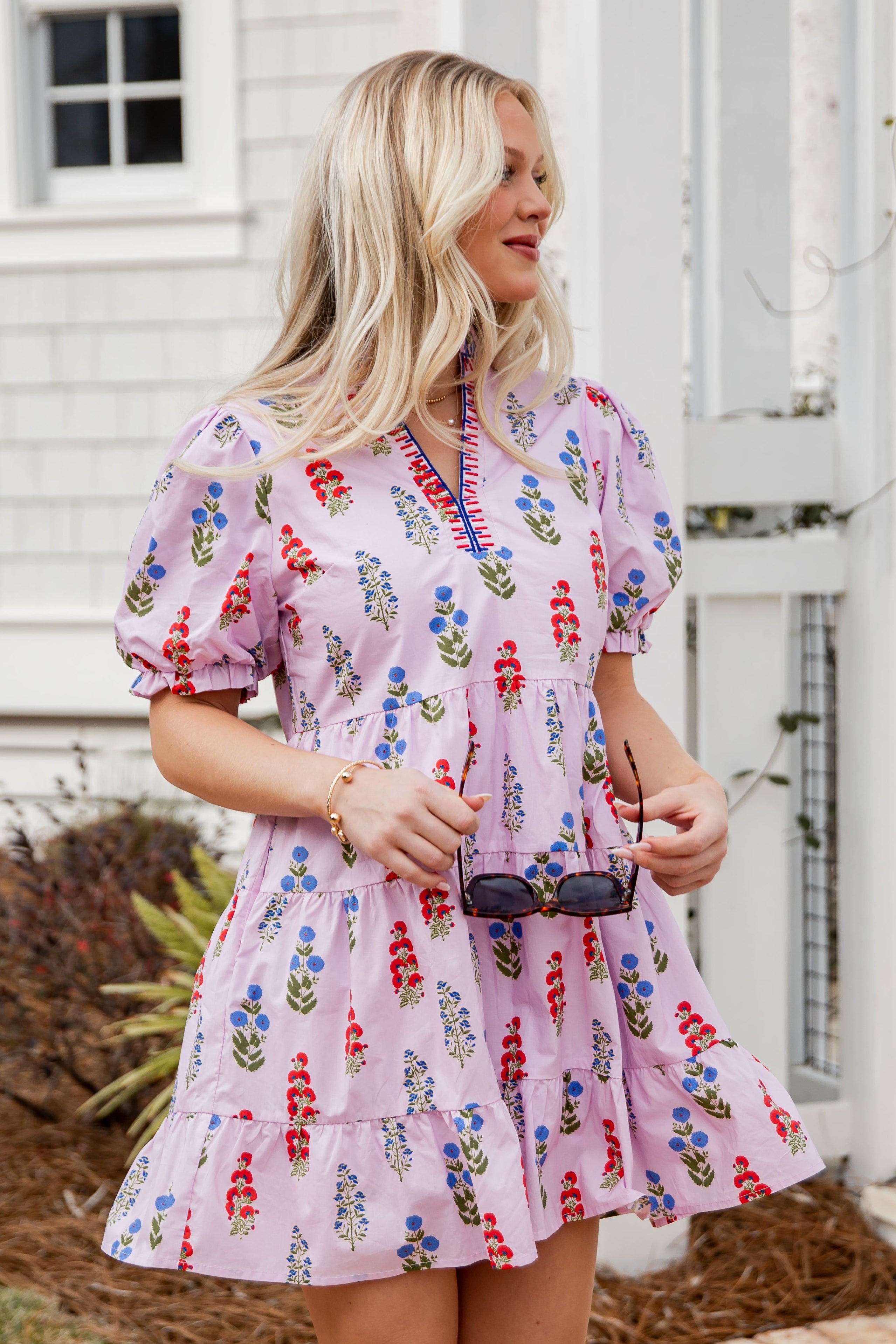Woman wearing a floral dress standing outdoors near a white building.