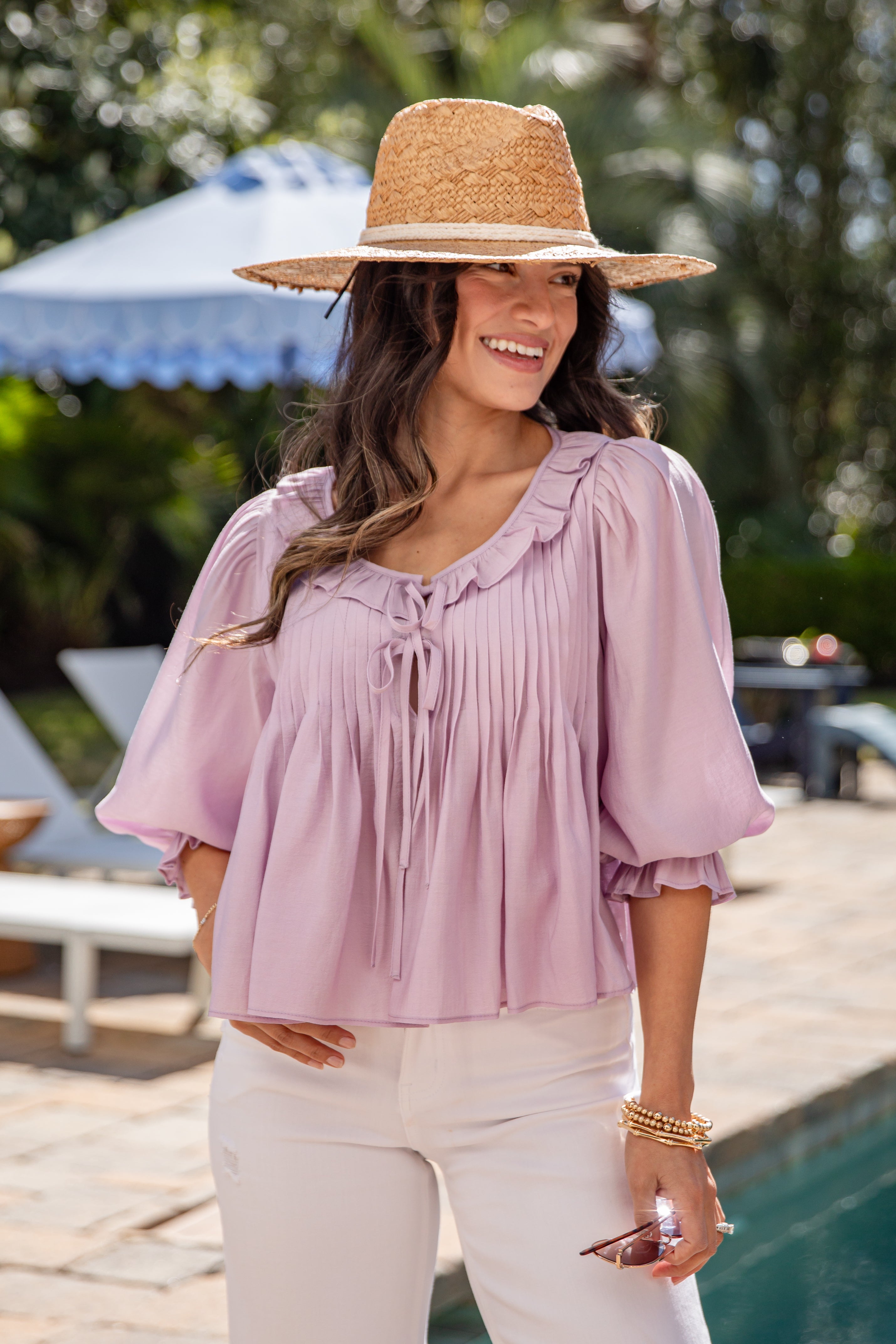 Woman wearing a pink blouse and straw hat by a poolside