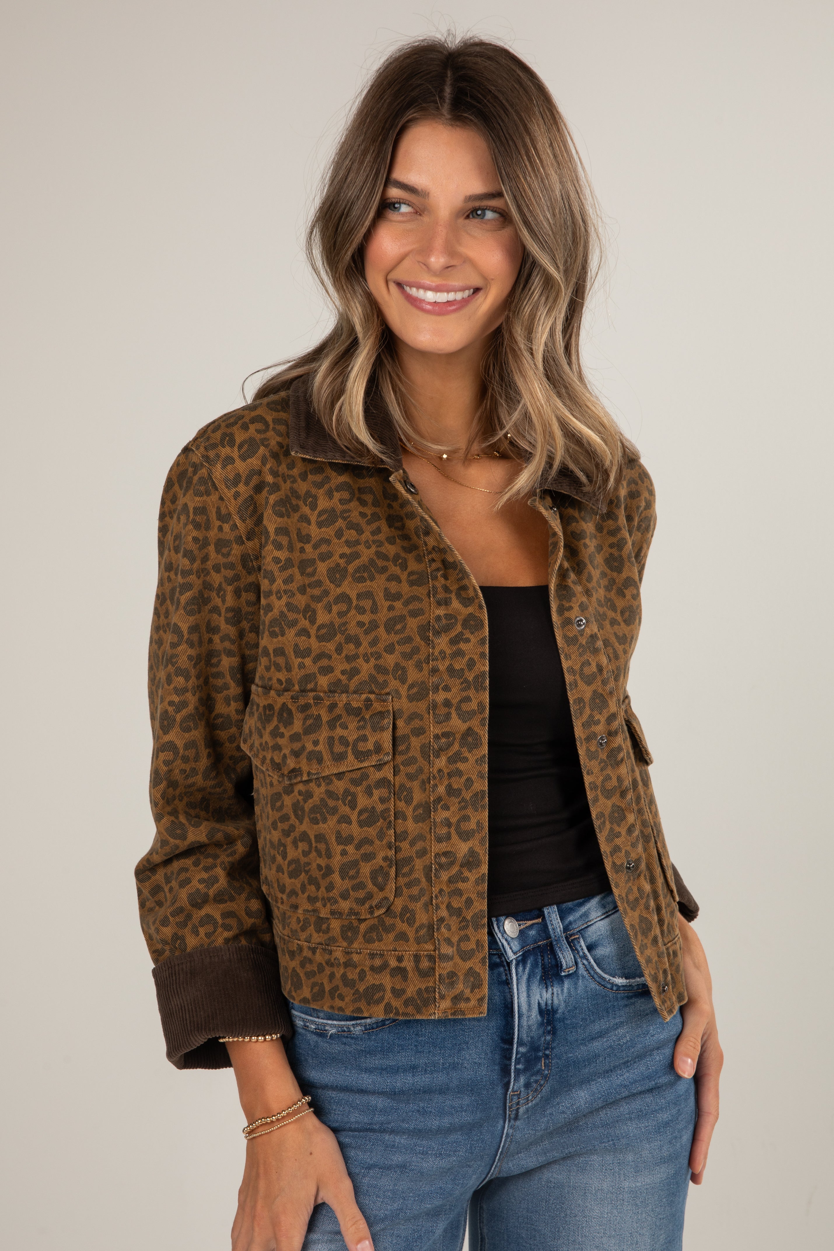Woman wearing a leopard print jacket, black top, and blue jeans on a plain background