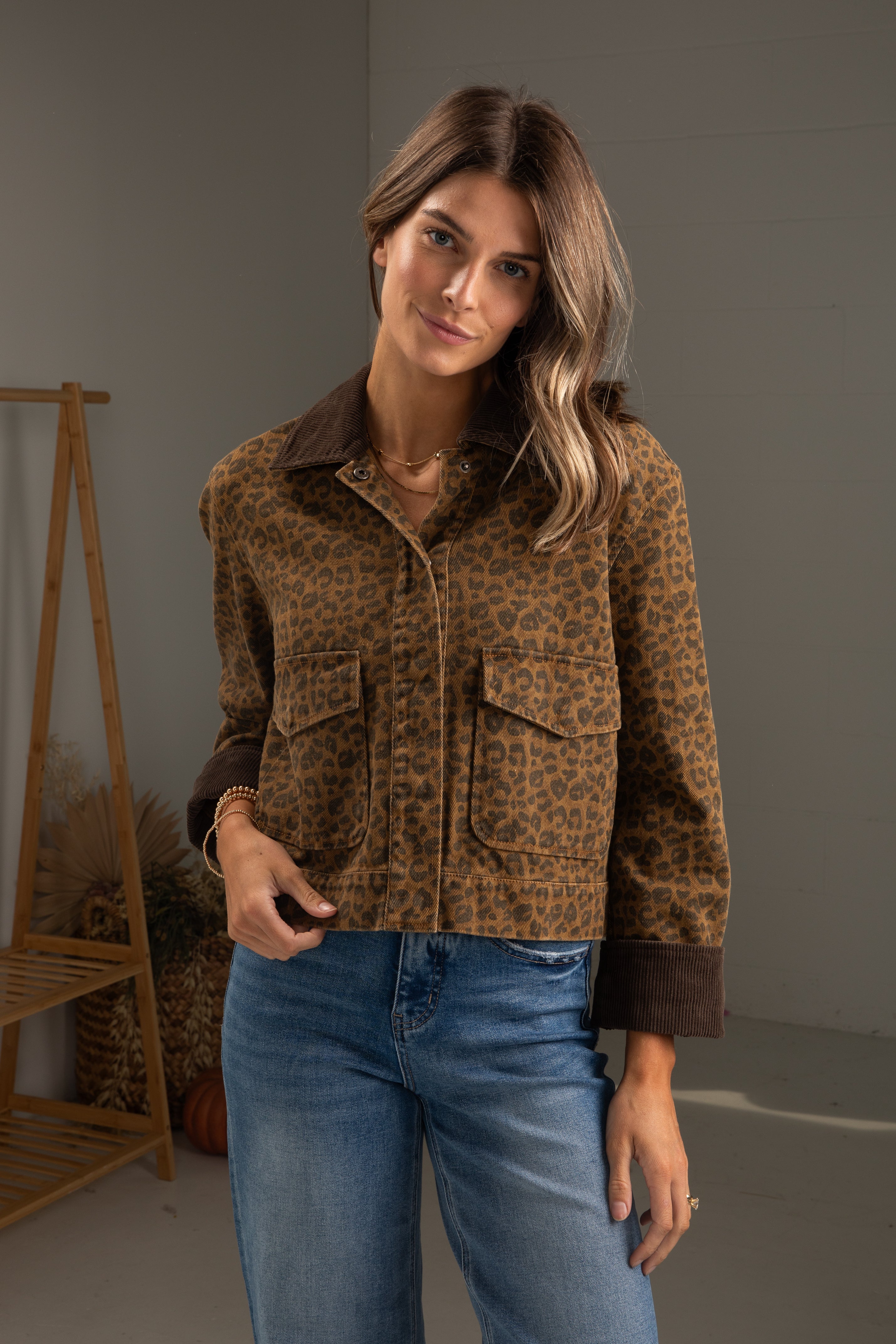 Woman wearing a leopard print jacket and blue jeans in a neutral setting