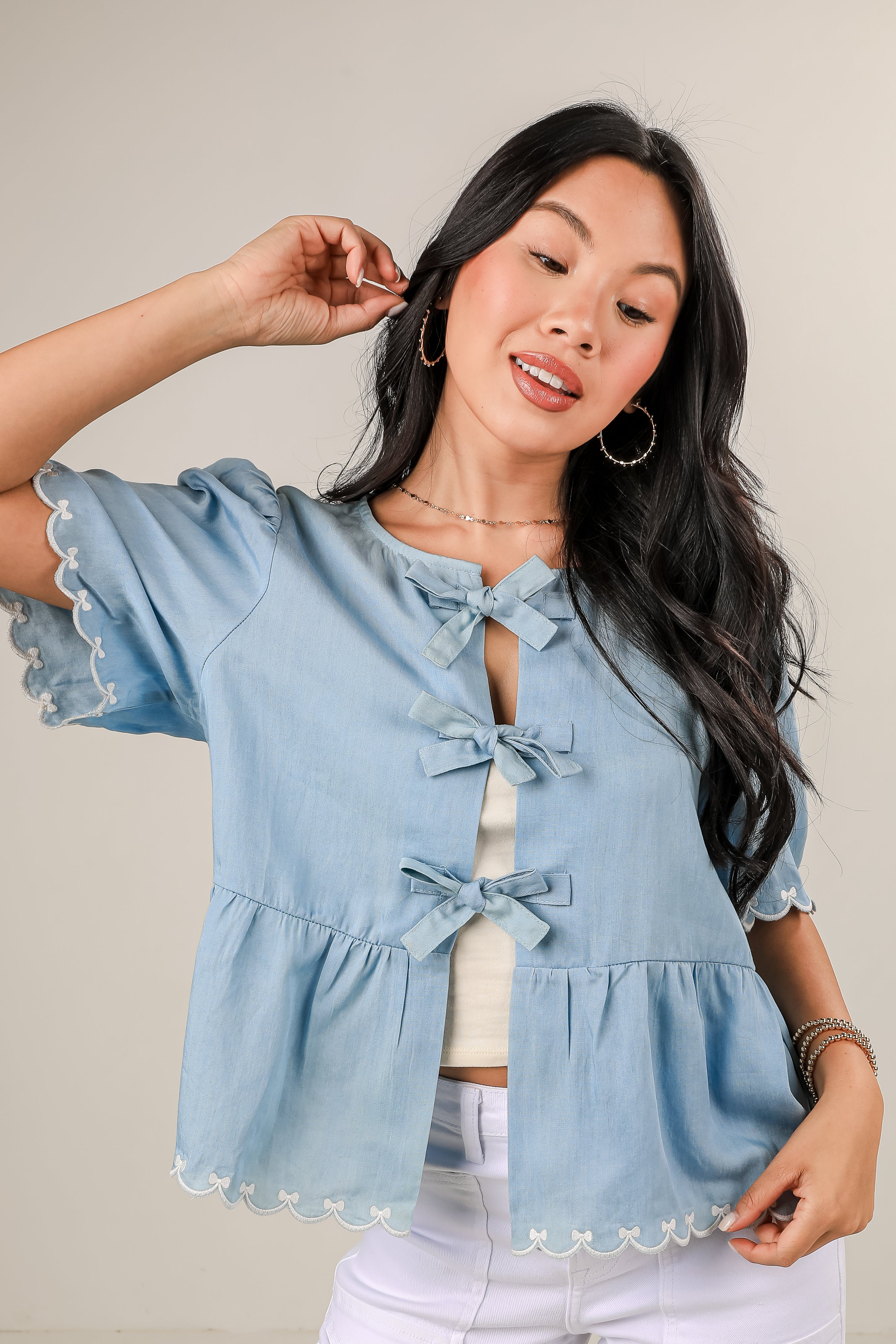 Woman wearing a light blue denim top with ruffled sleeves and hem on a plain background