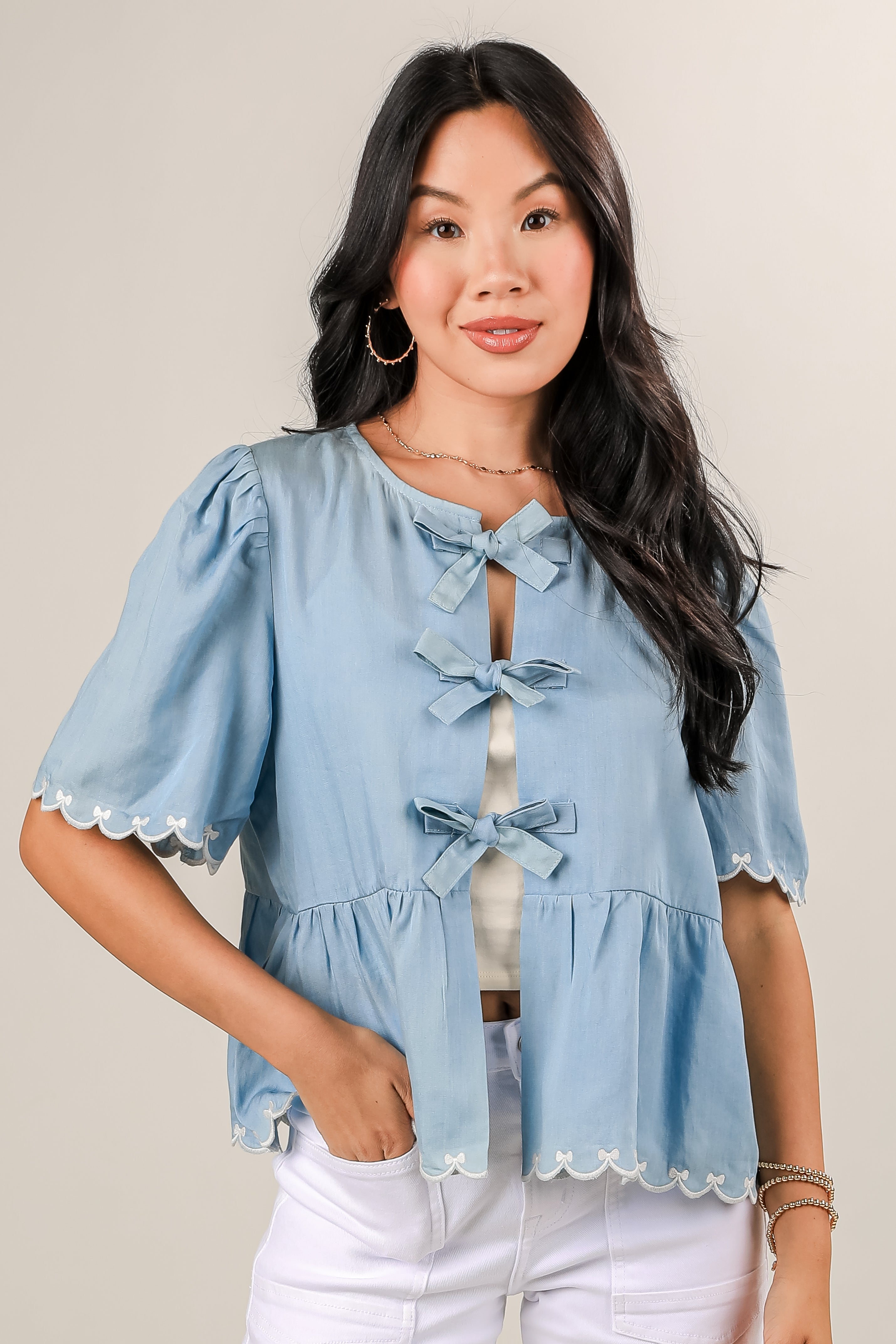 Woman wearing a light blue blouse with lace details on a plain background
