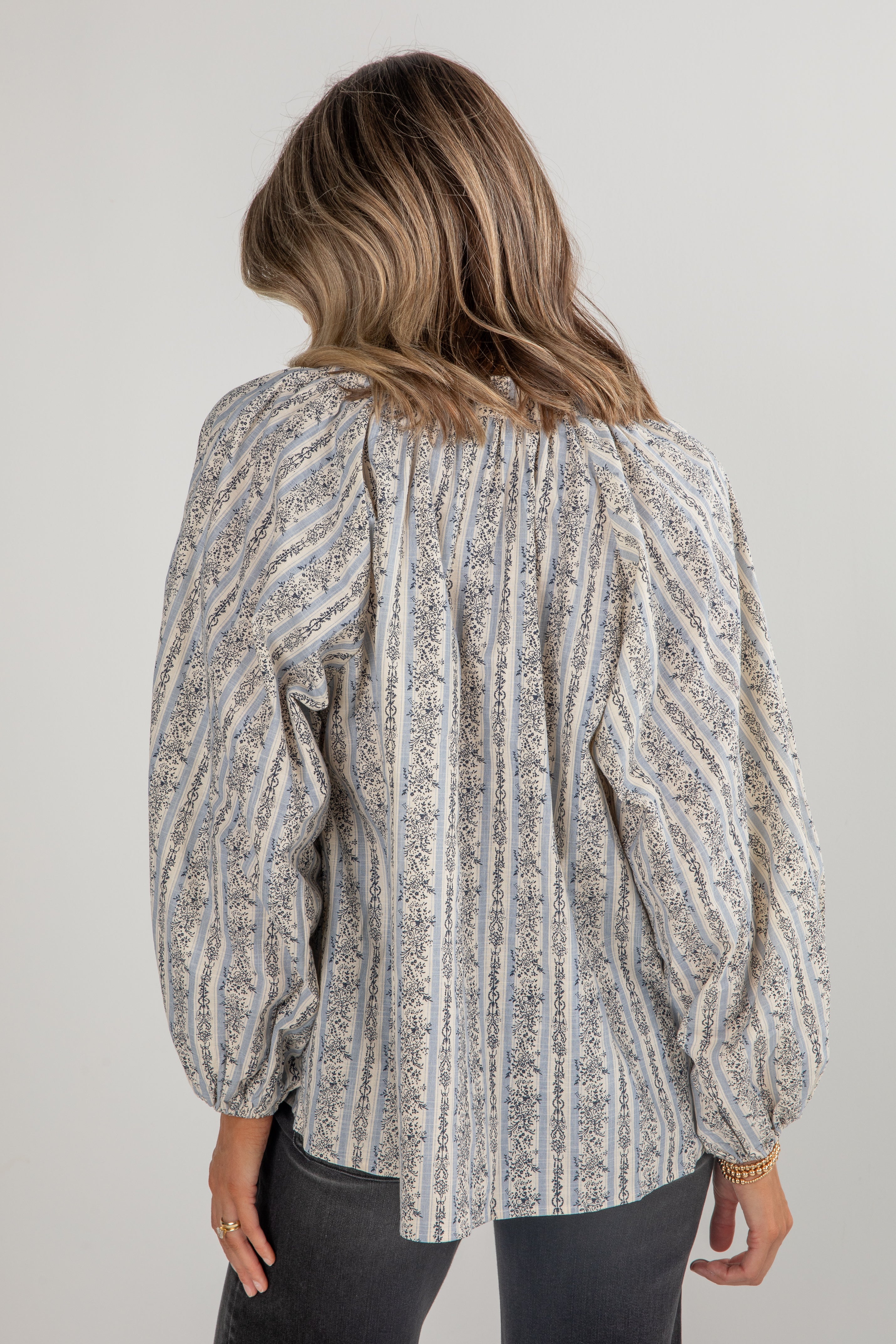 Woman wearing a patterned blouse with long sleeves on a plain background