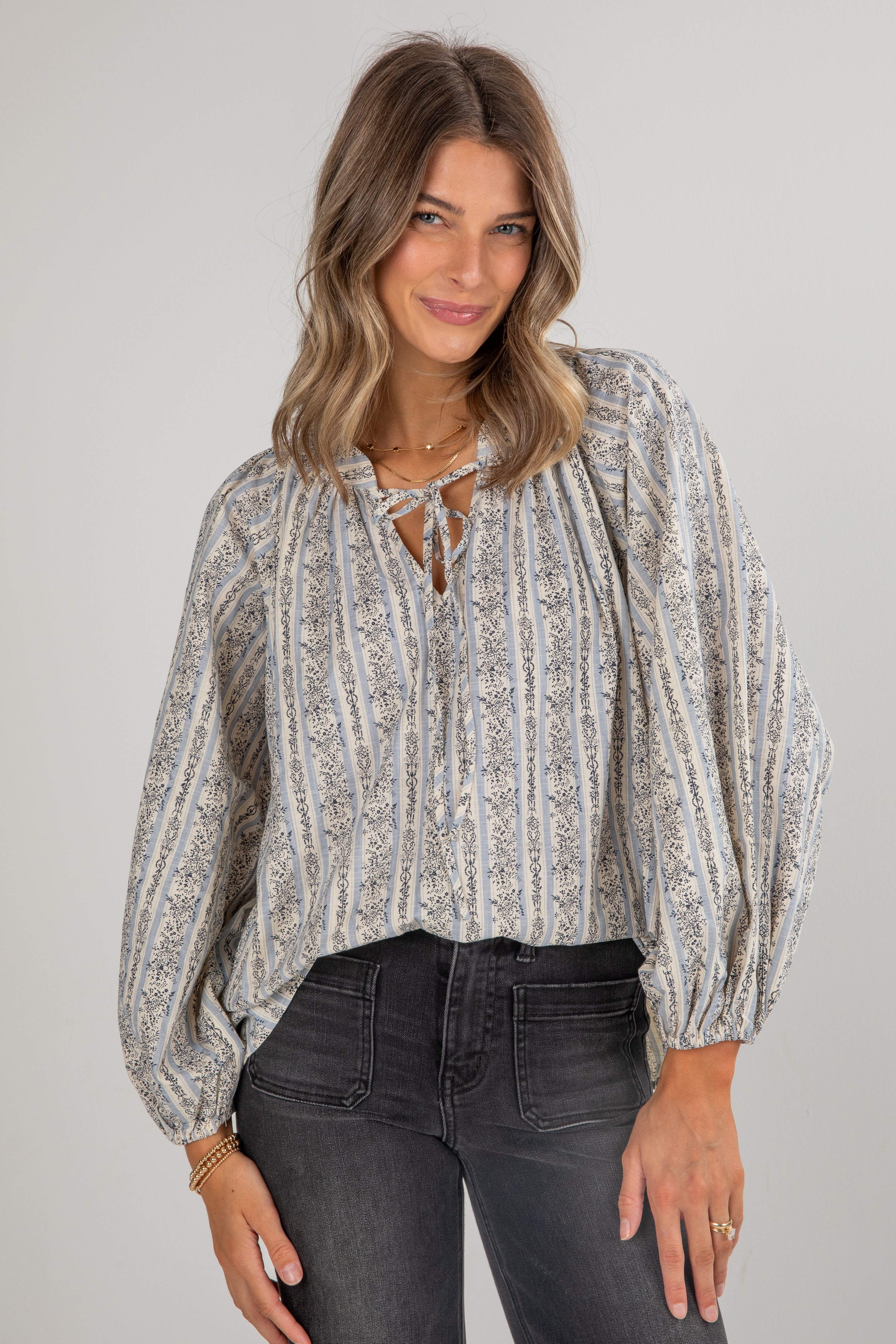 Woman wearing a patterned blouse and dark jeans against a plain background