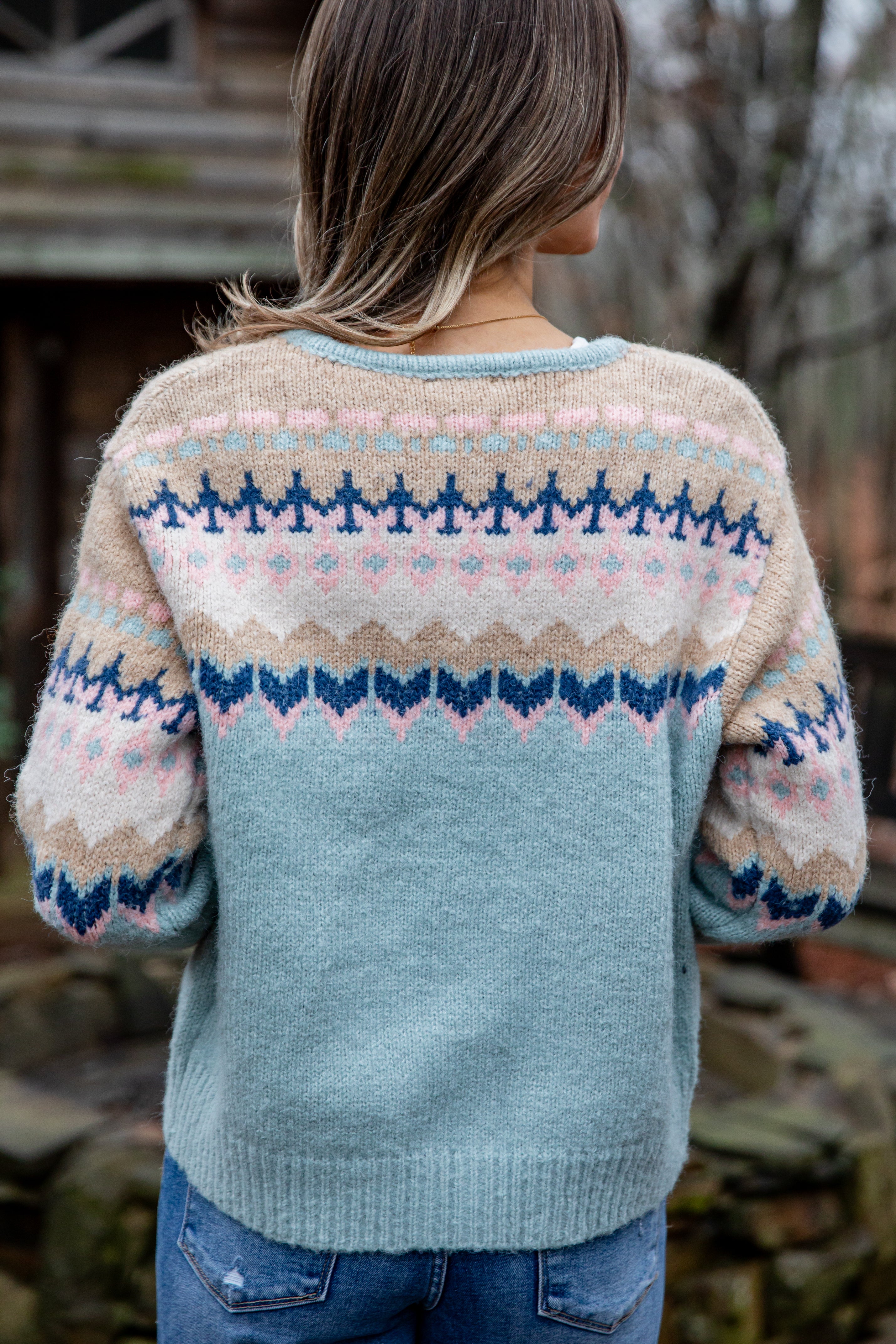 Person wearing a patterned sweater with a blurred natural background