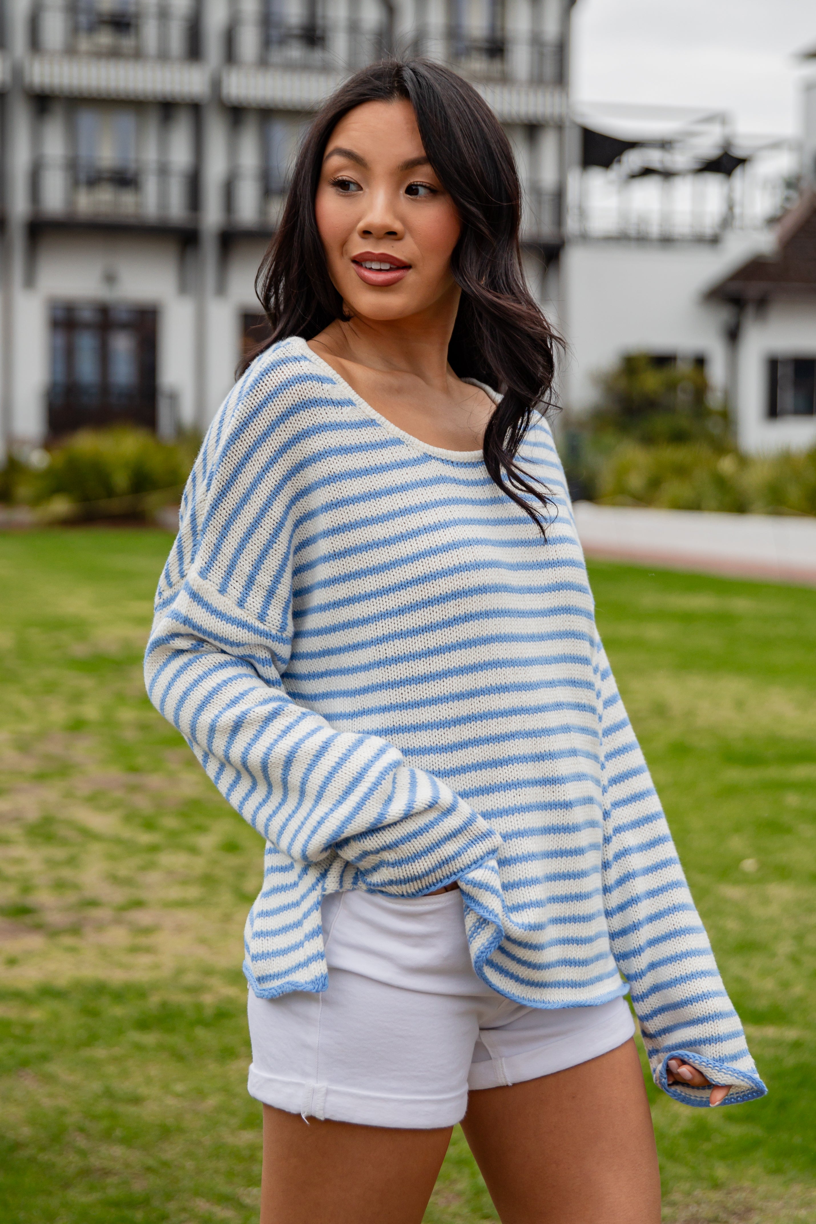 Woman wearing a blue and white striped sweater and white shorts outdoors.