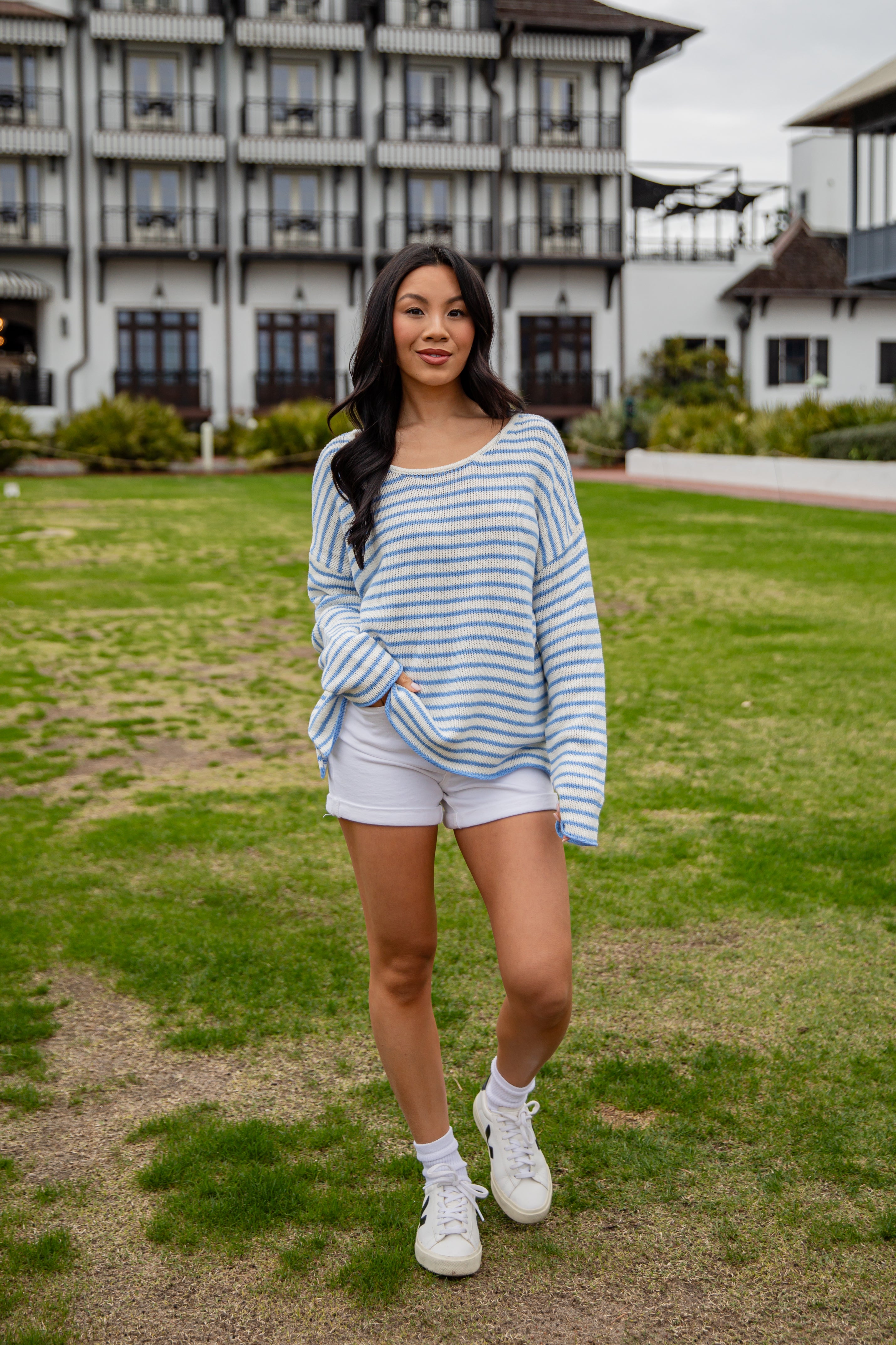 Woman in a striped sweater and shorts standing on grass with a building in the background