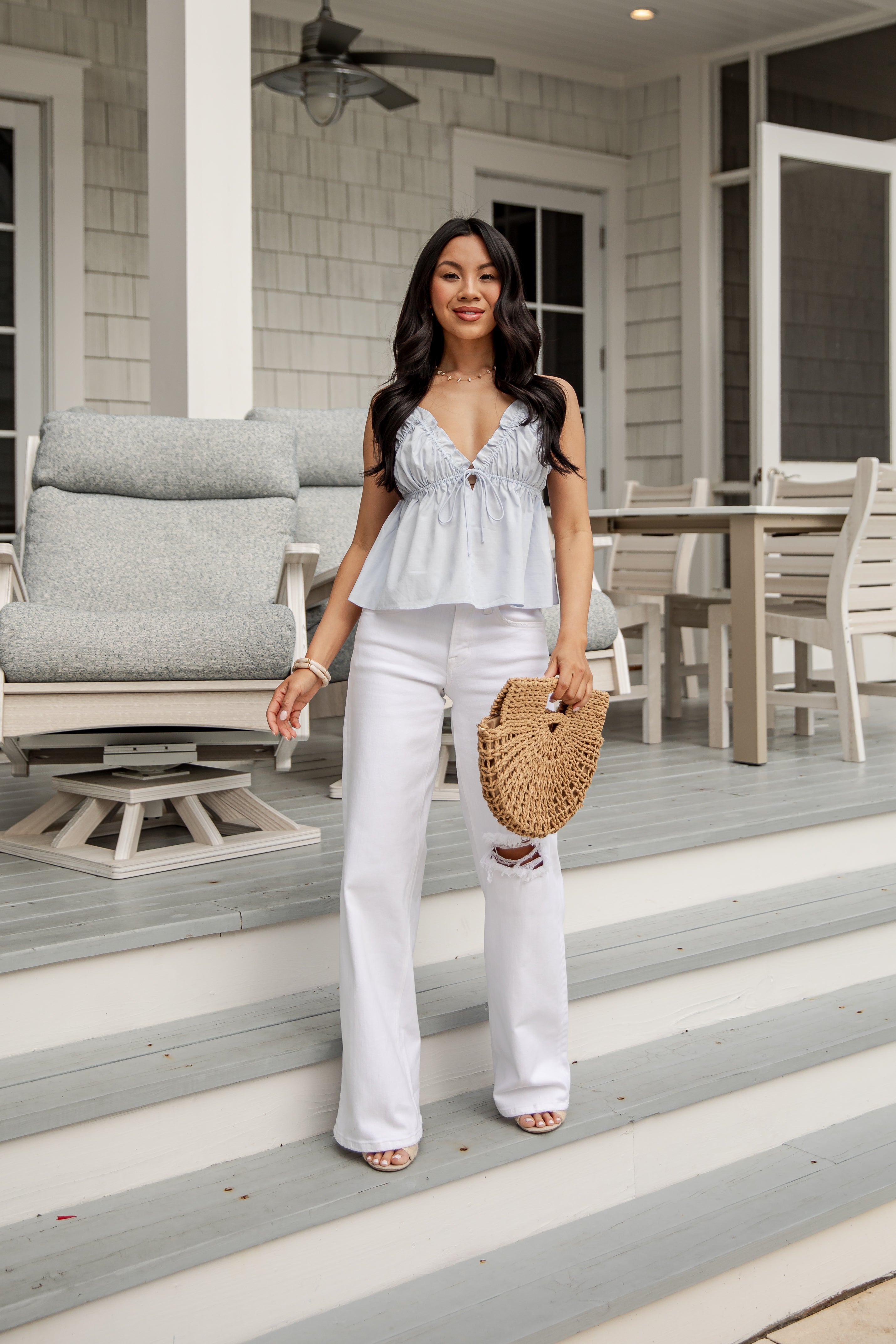 Woman in white outfit holding a straw bag on a porch