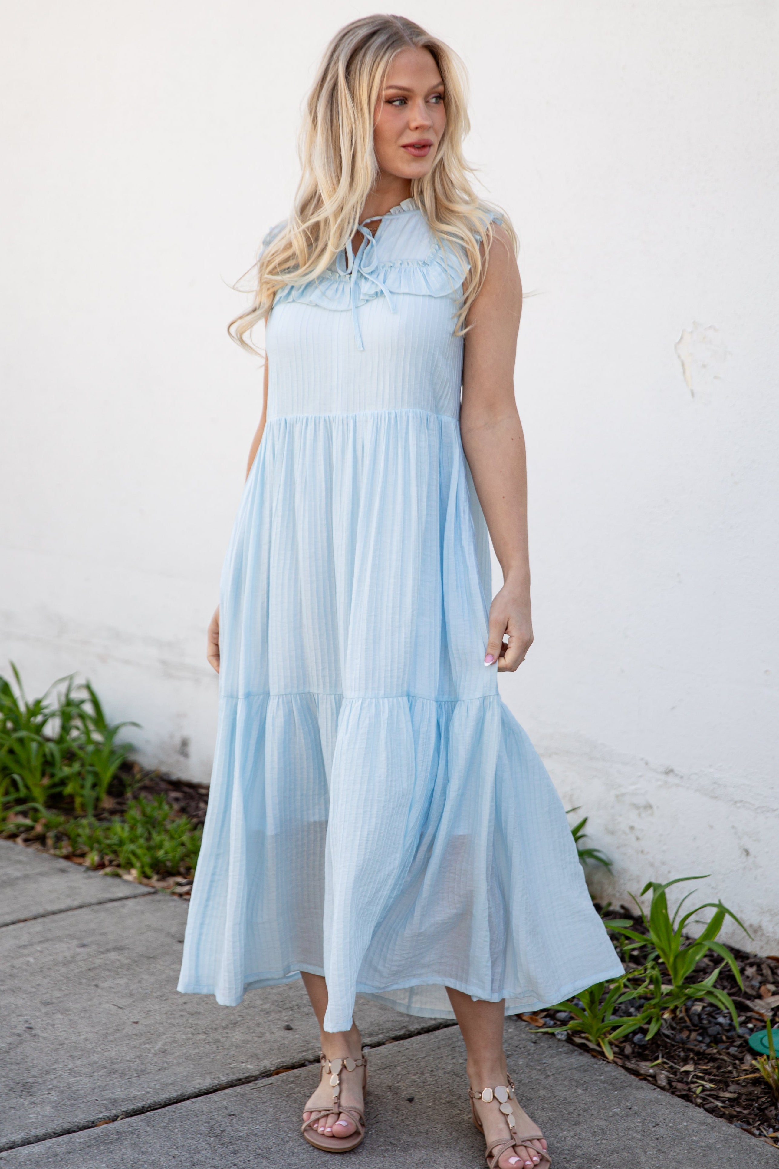 Woman wearing a light blue dress standing against a white wall.