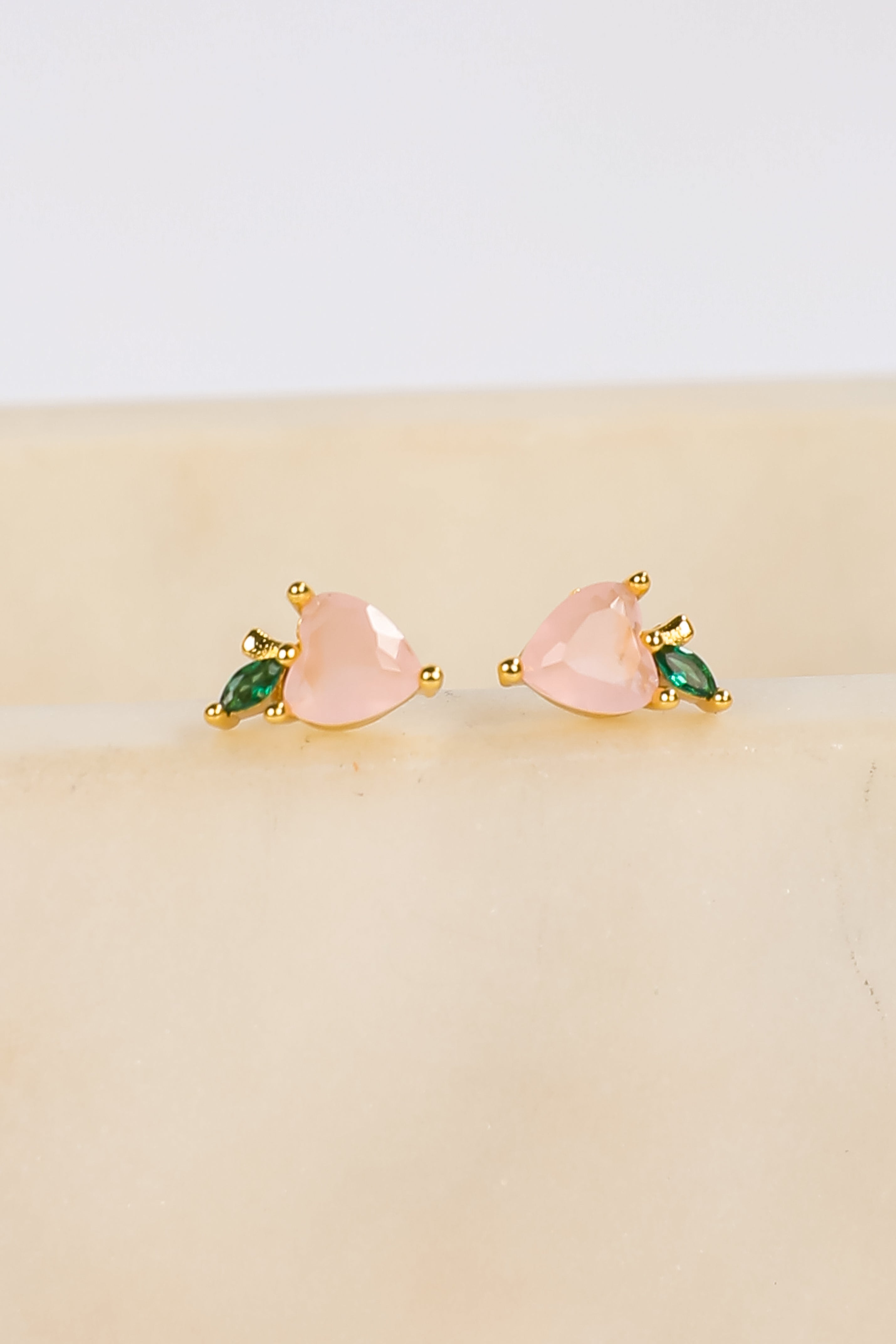Pair of heart-shaped earrings with green accents on a beige surface.