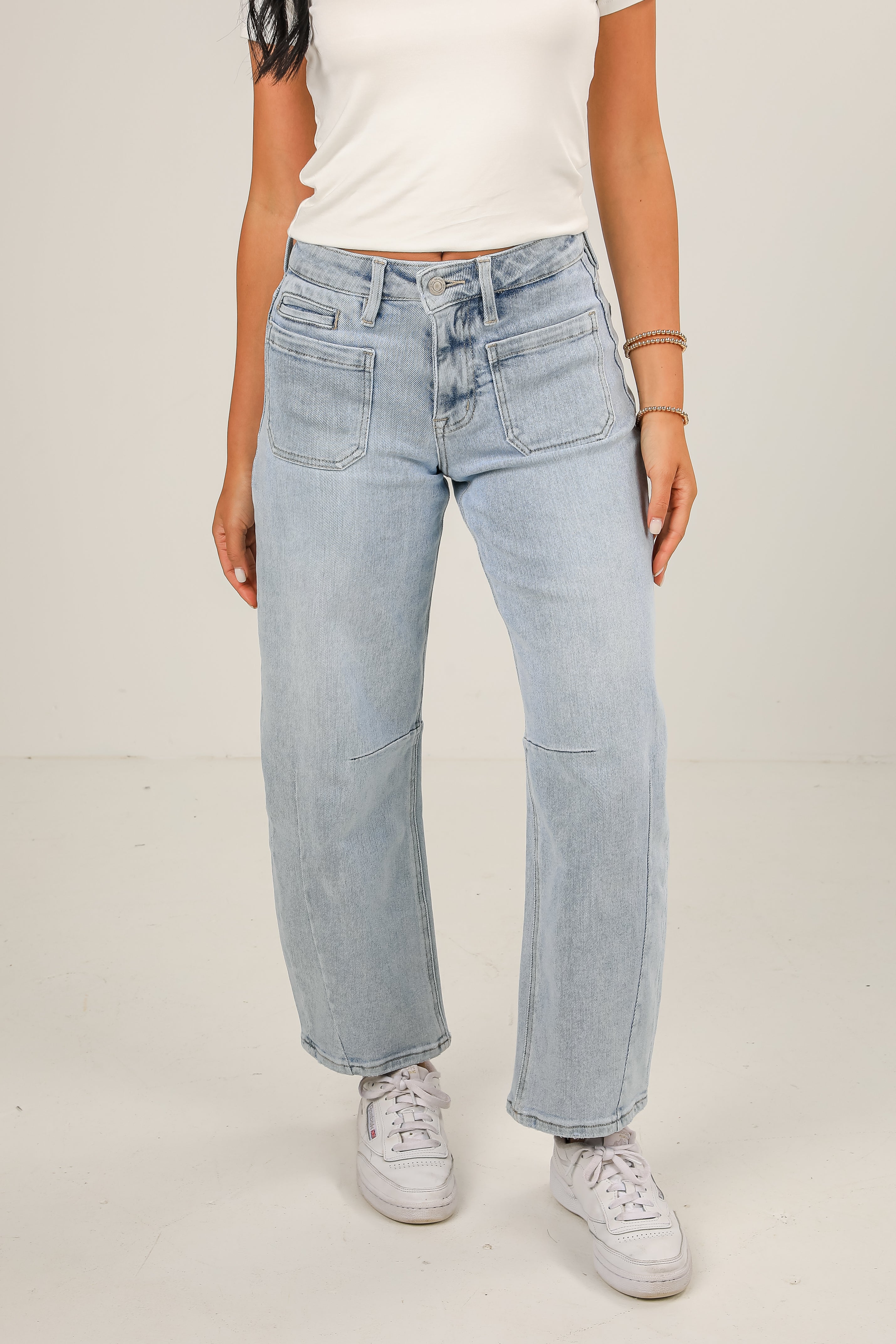 Person wearing light blue jeans and white sneakers on a plain background