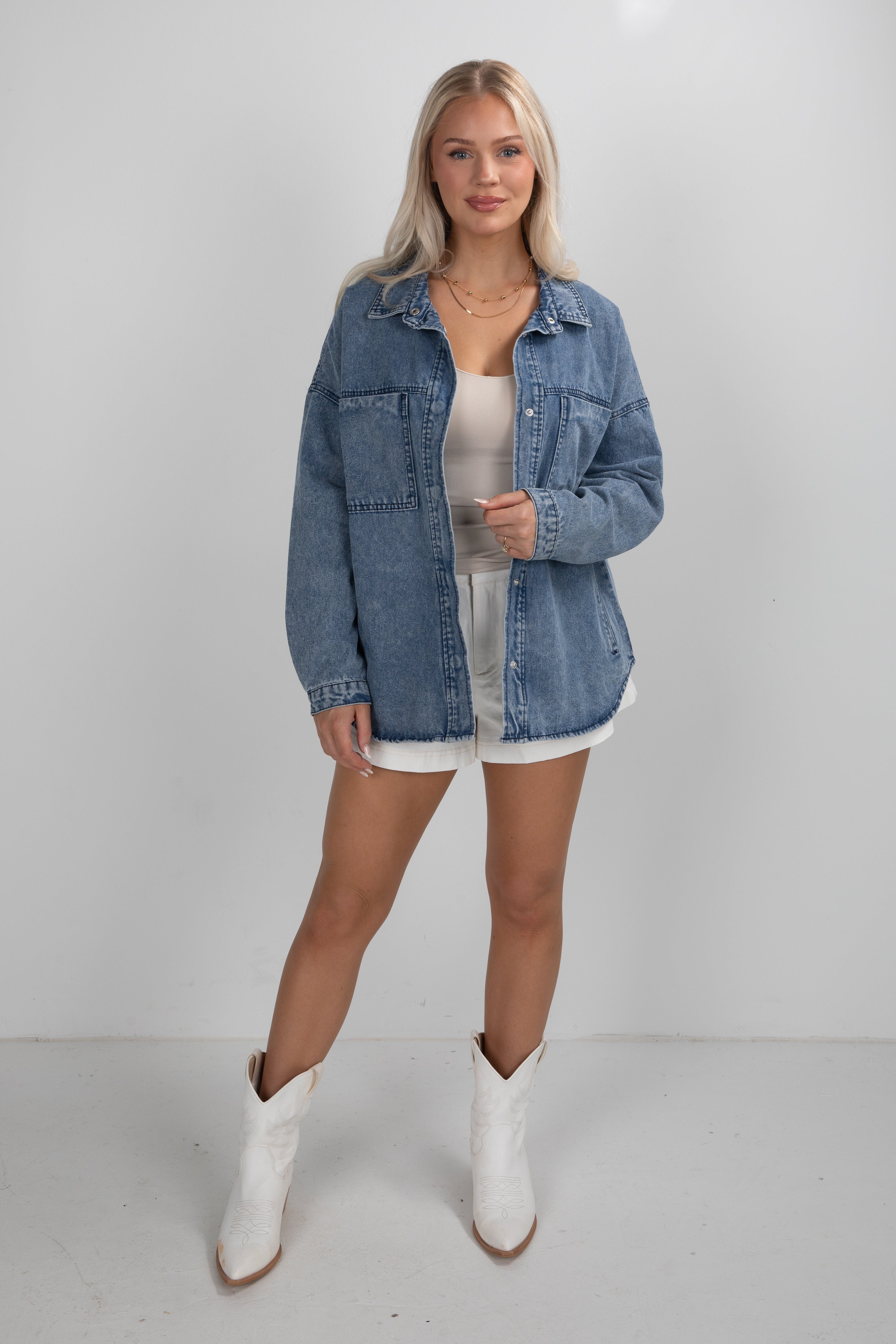 Woman wearing a denim jacket, white dress, and white boots on a plain background