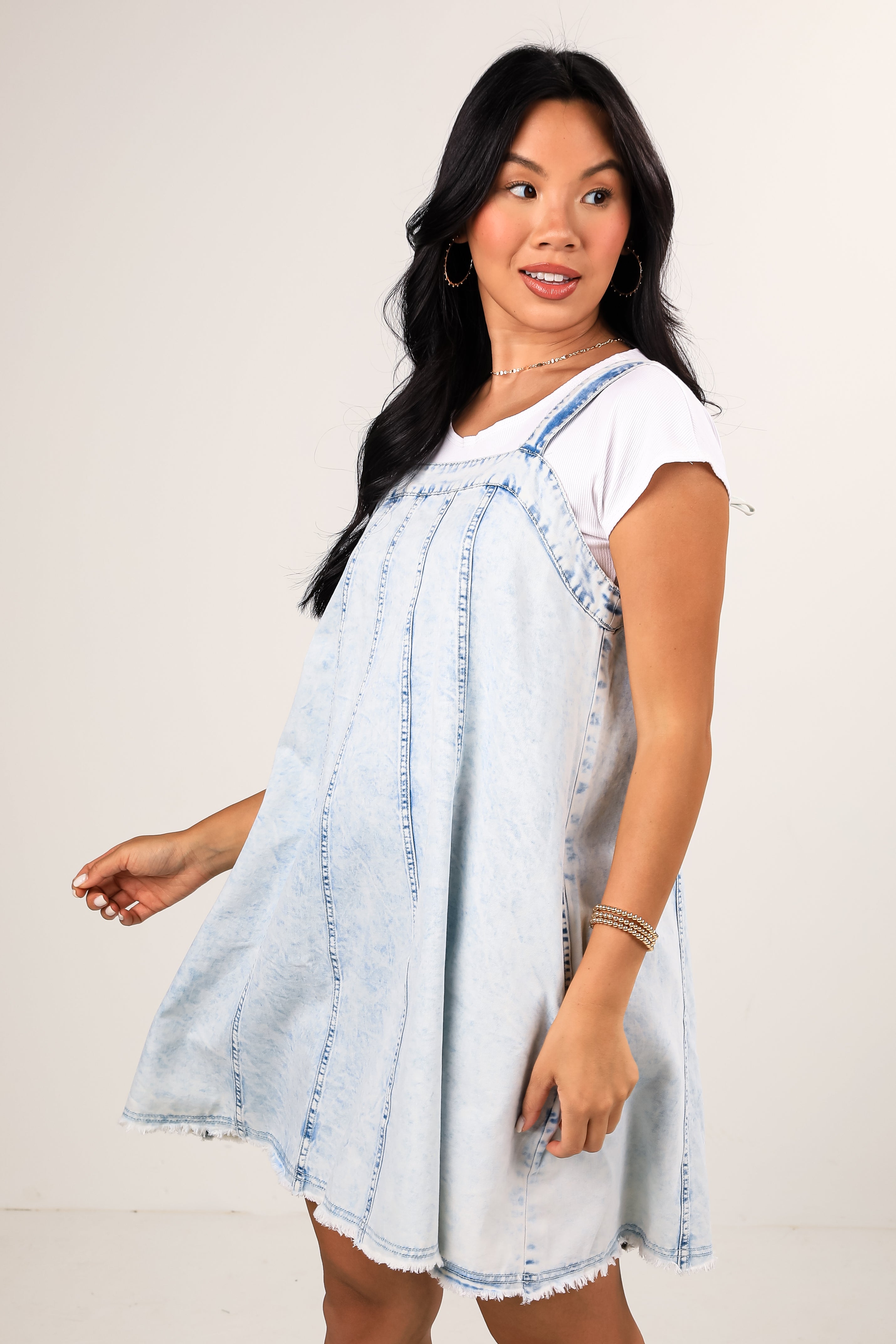 Woman wearing a light blue denim dress over a white t-shirt against a plain background