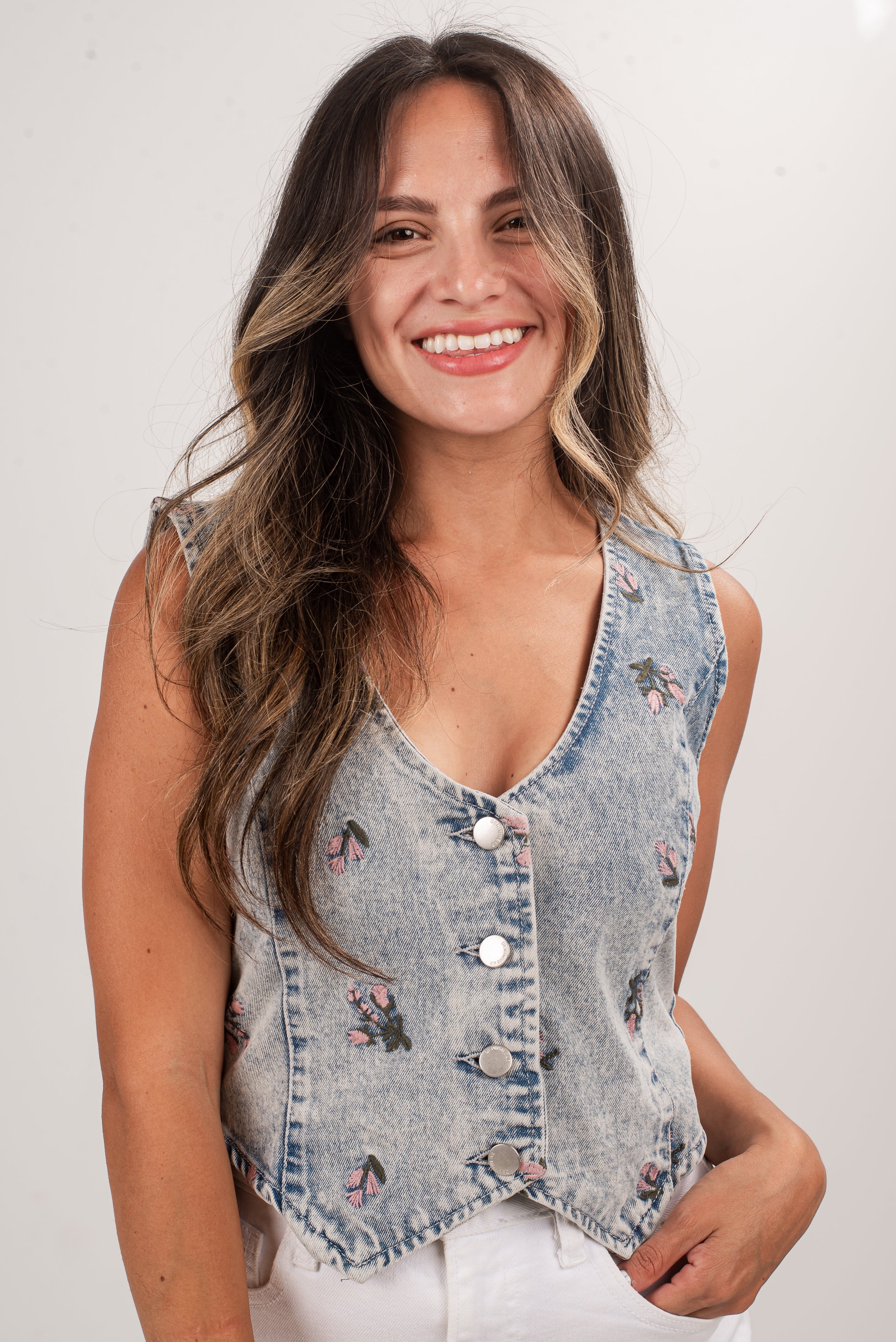 Woman wearing a denim vest with floral embroidery on a white background