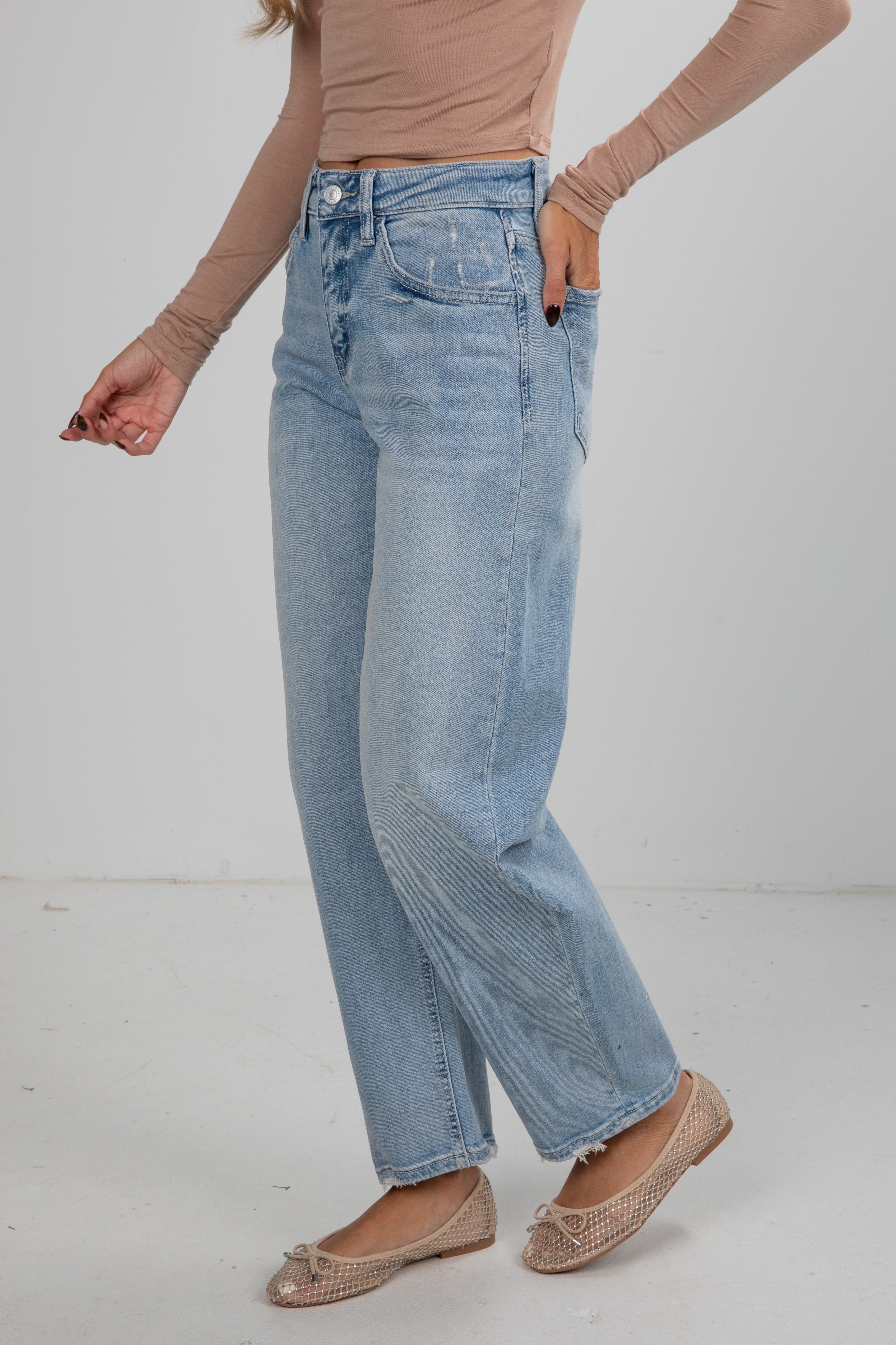 Person wearing light blue jeans and a beige top on a white background
