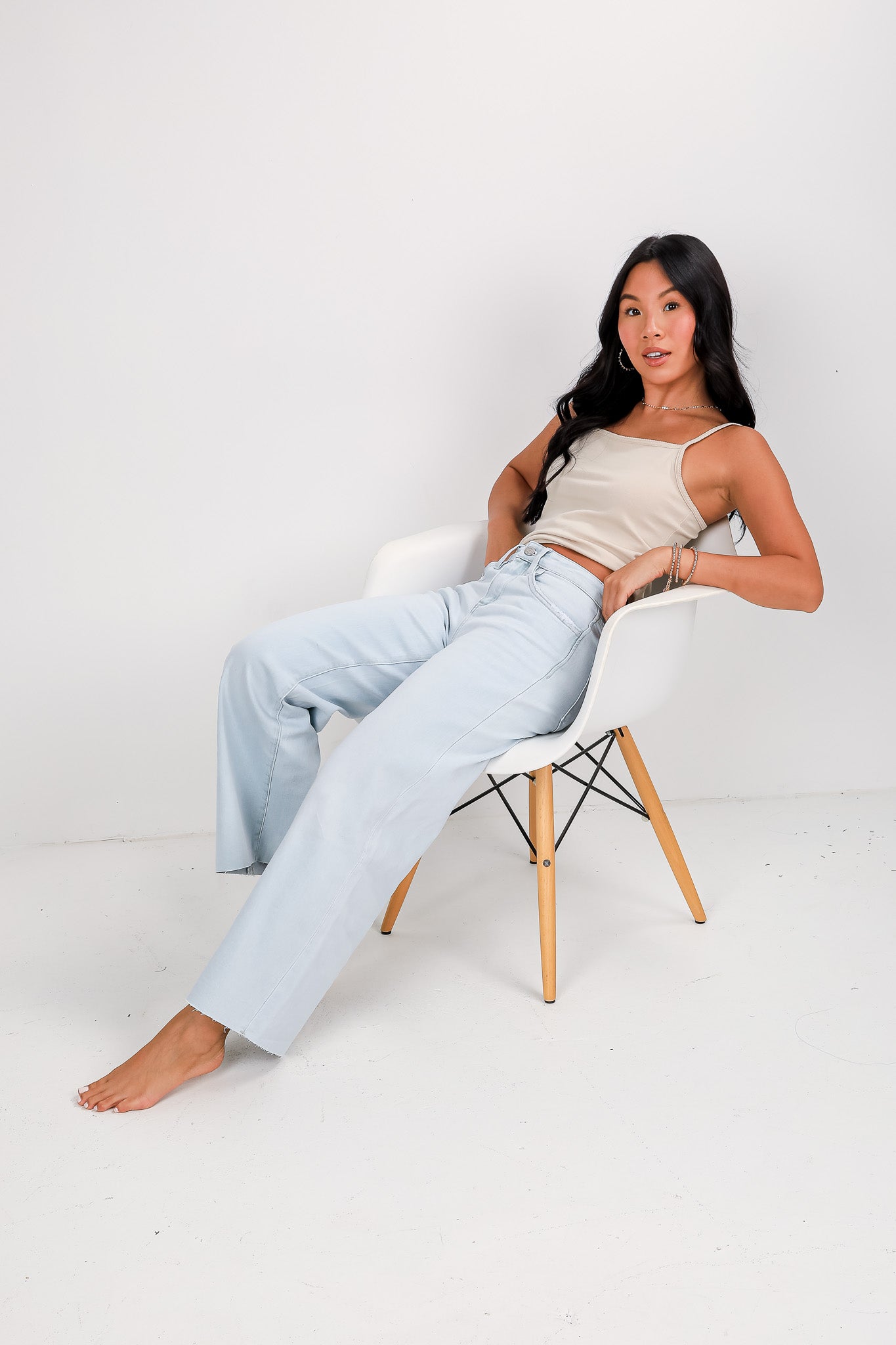 Woman sitting on a chair wearing light blue jeans and a beige top against a white background