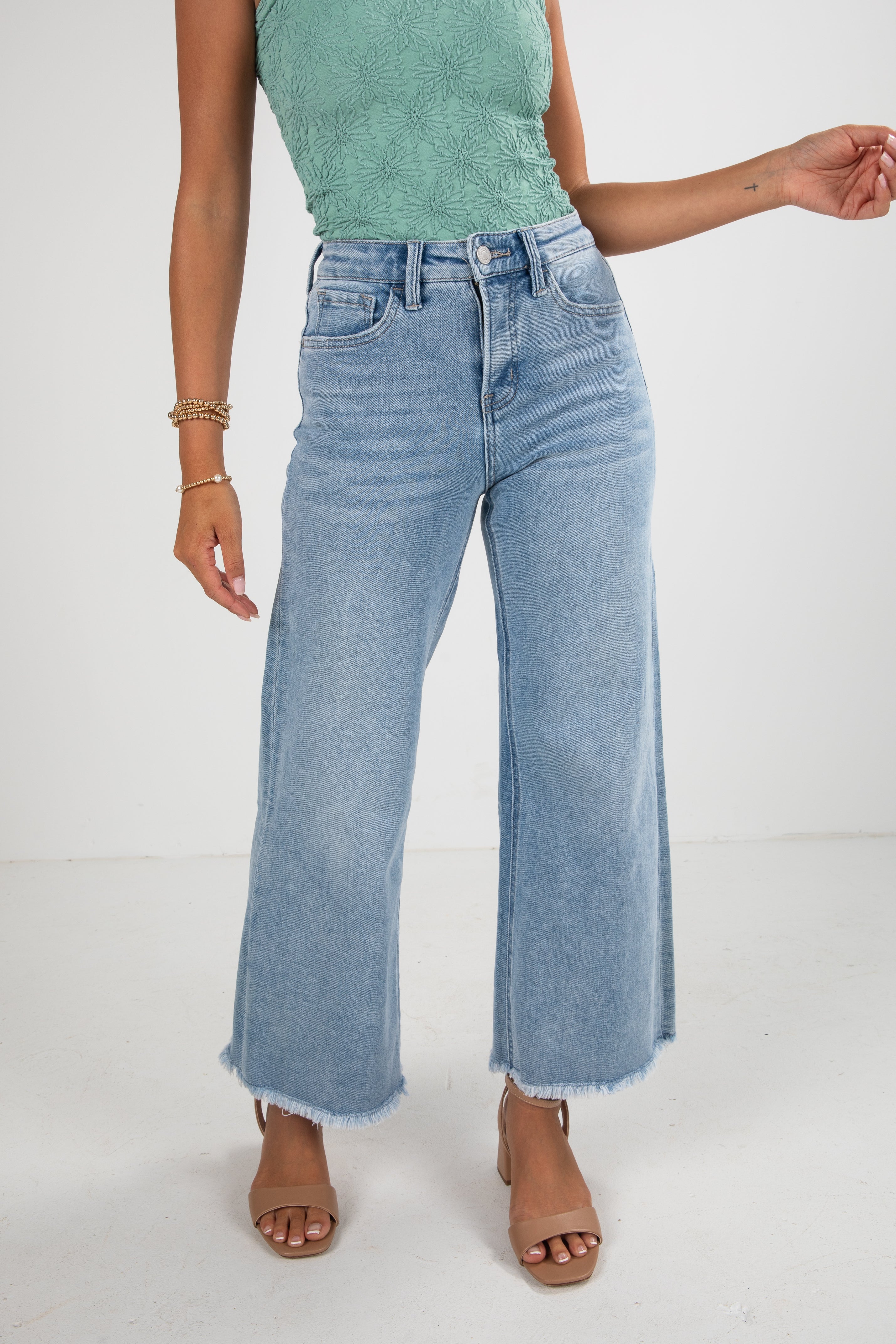 Person wearing light blue jeans and a green top on a white background