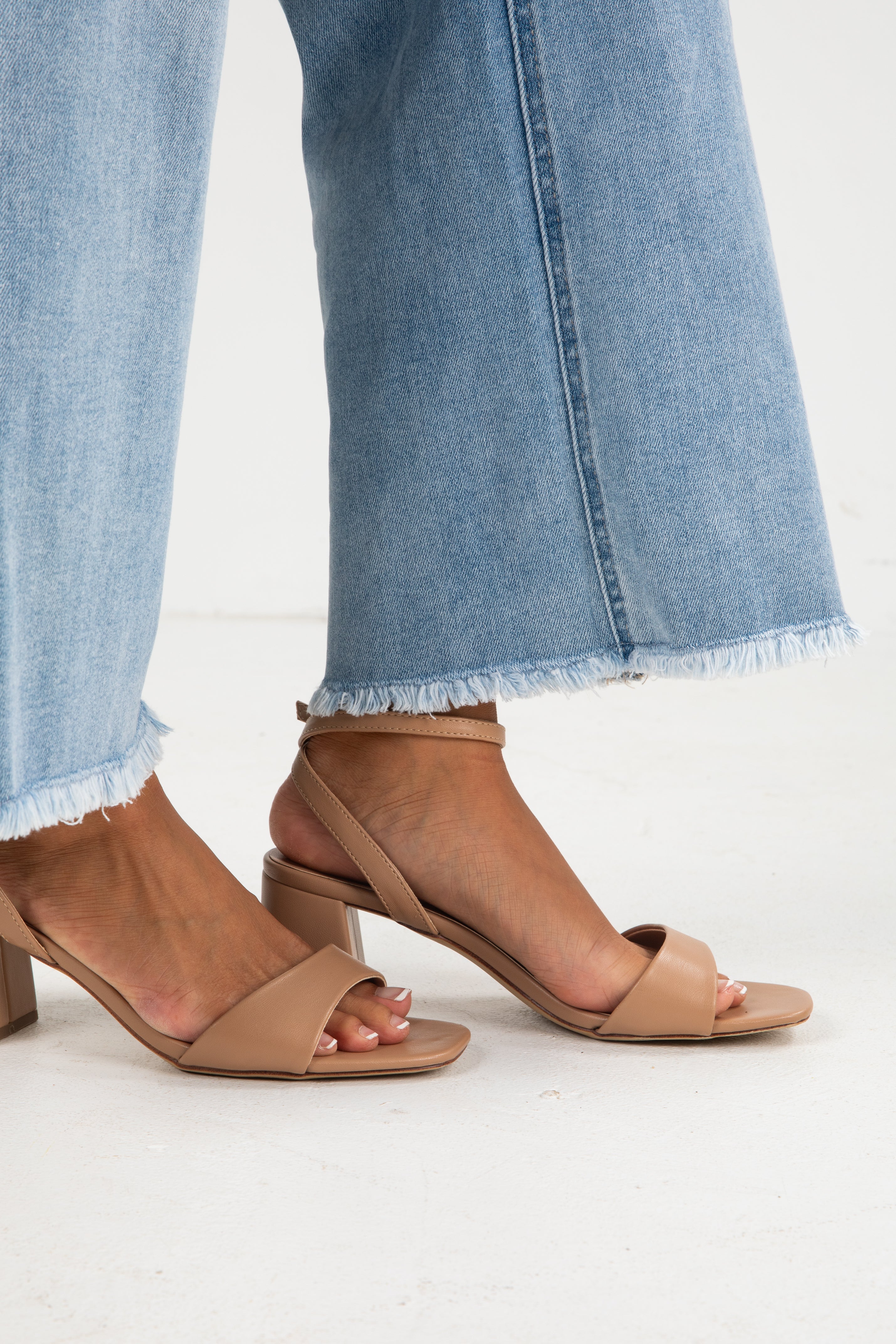 Tan high-heeled sandals worn with light blue jeans on a white background