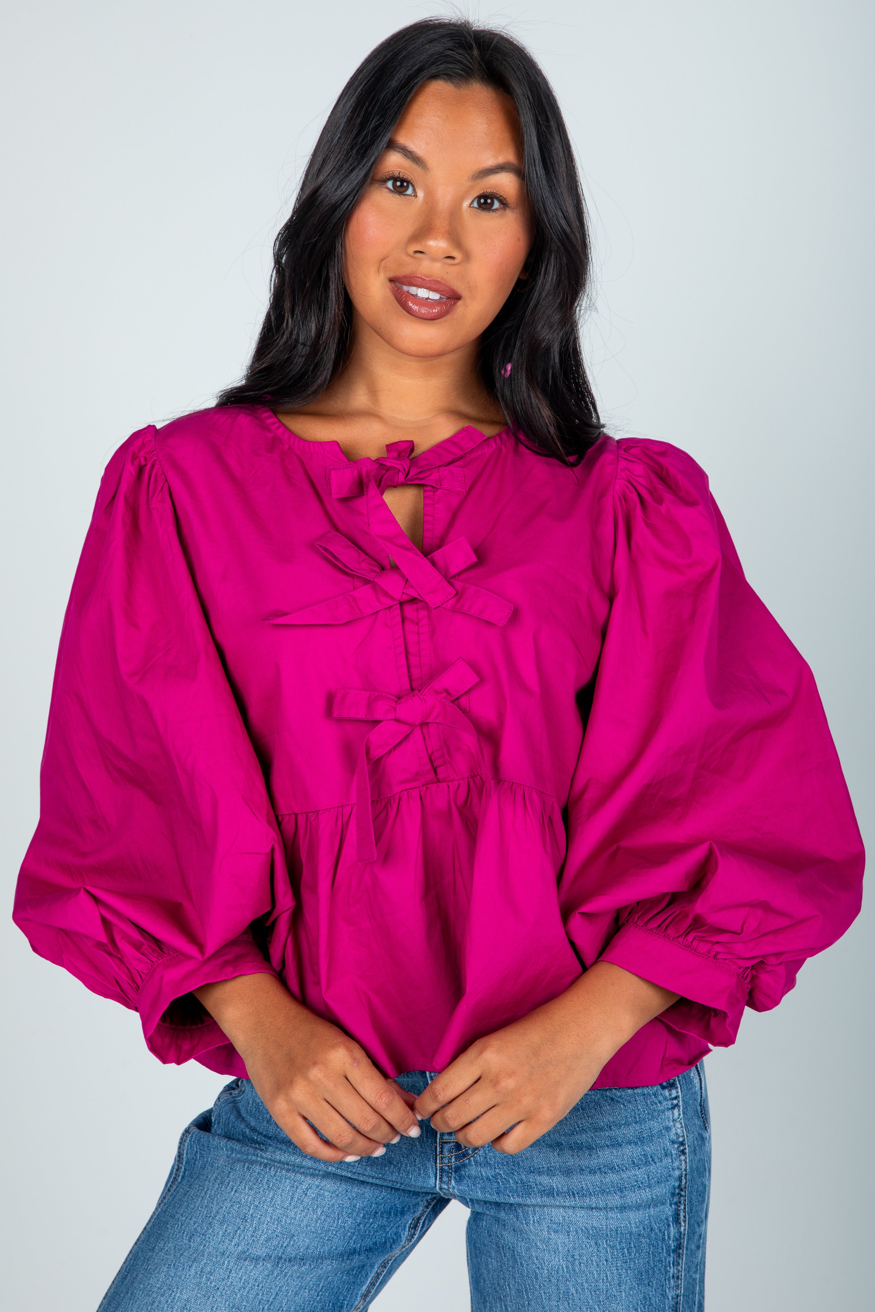 Woman wearing a bright pink blouse with puffed sleeves against a plain background