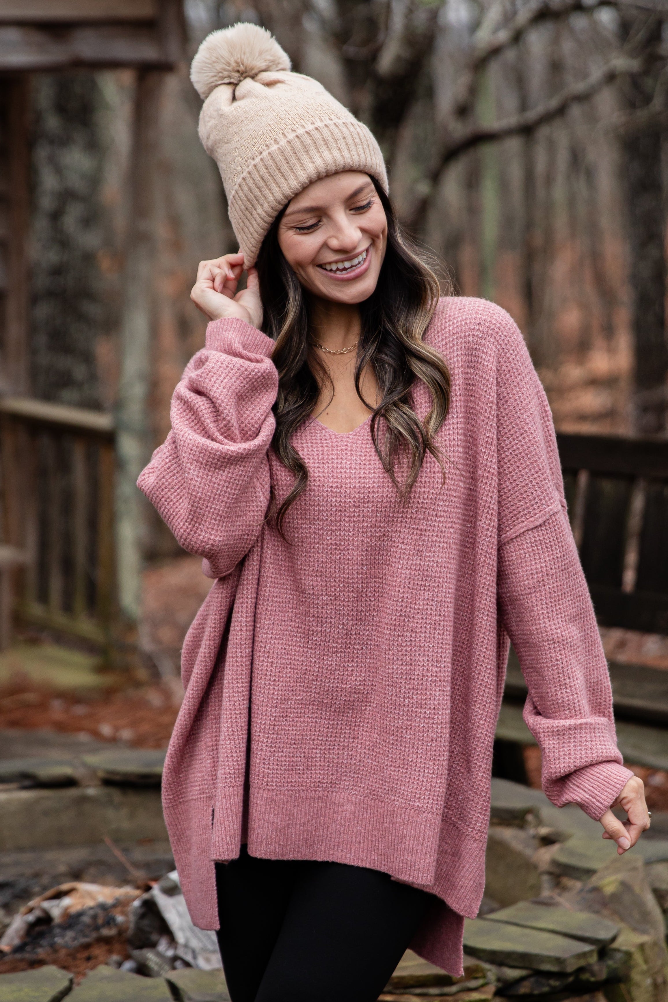 Woman wearing a pink sweater and beanie standing near a fire pit.