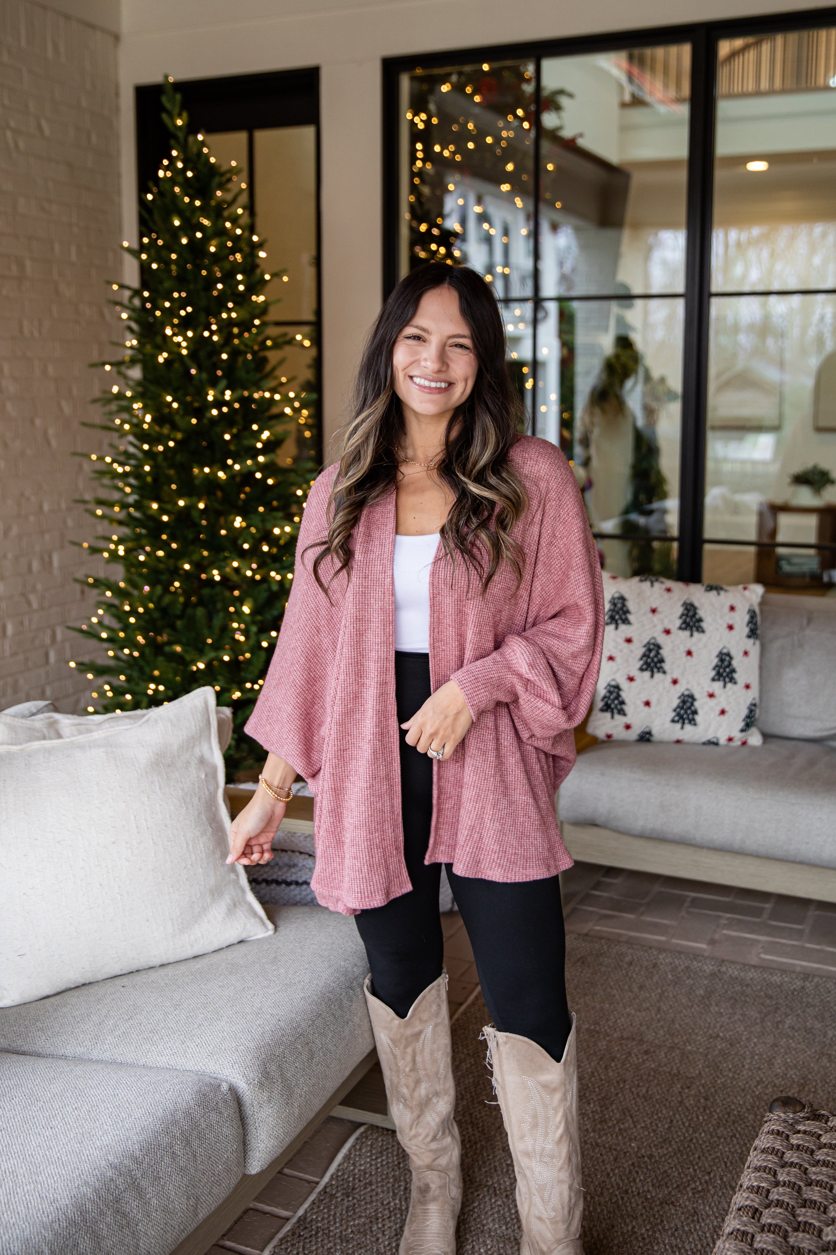 Woman in a pink cardigan standing in a living room with a Christmas tree.