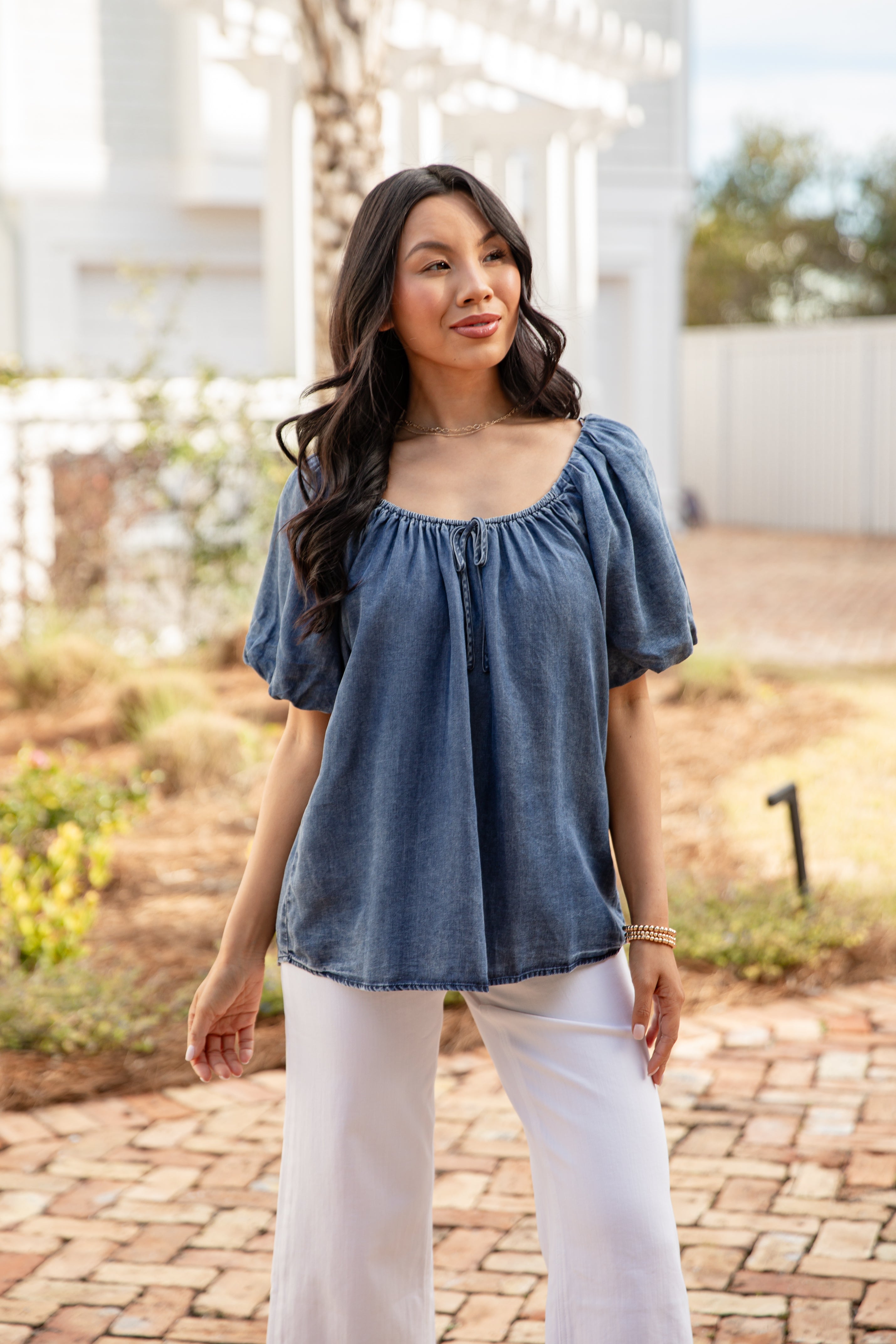 Woman wearing a blue top and white pants standing outdoors.