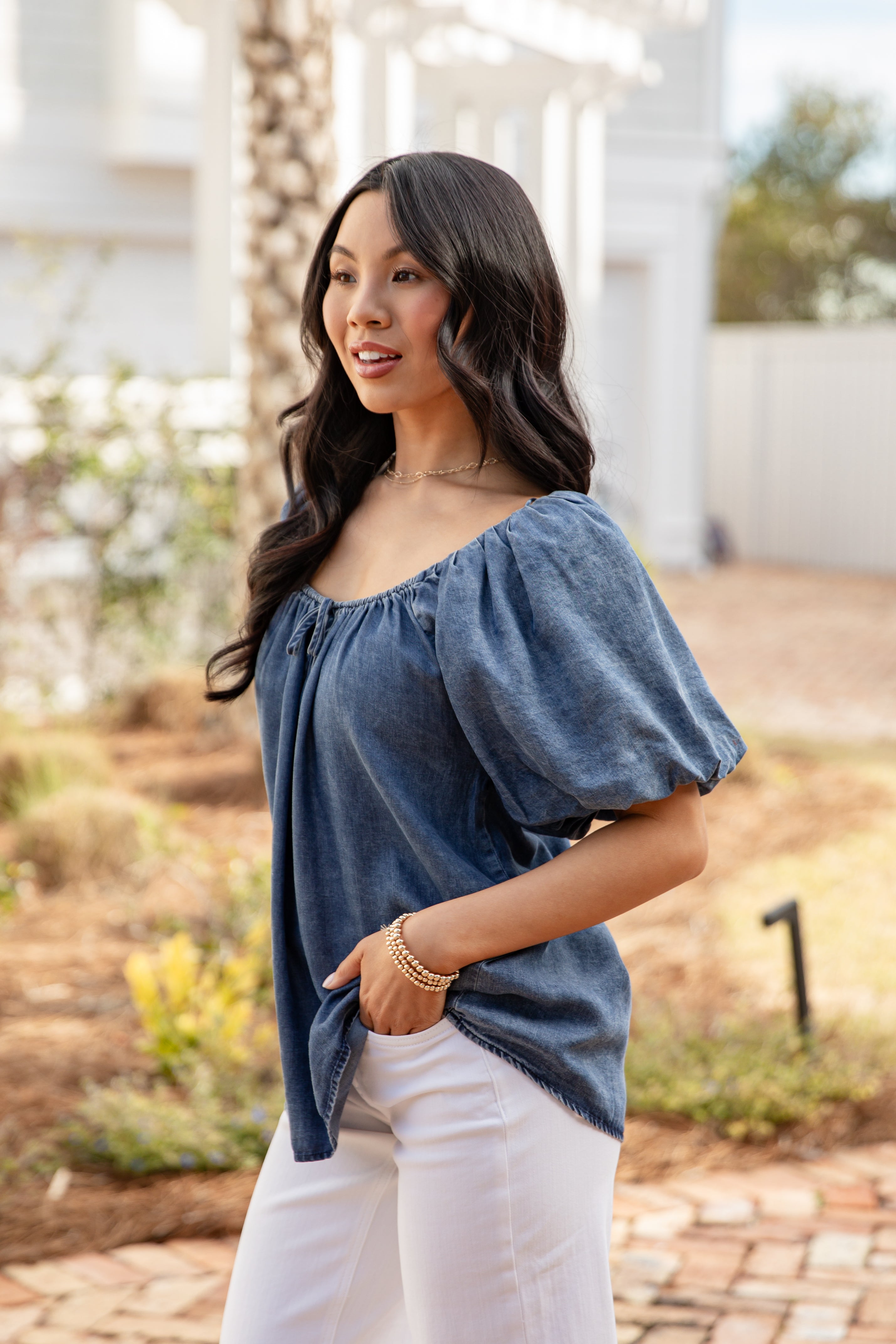 Woman wearing a blue top and white pants standing outdoors.
