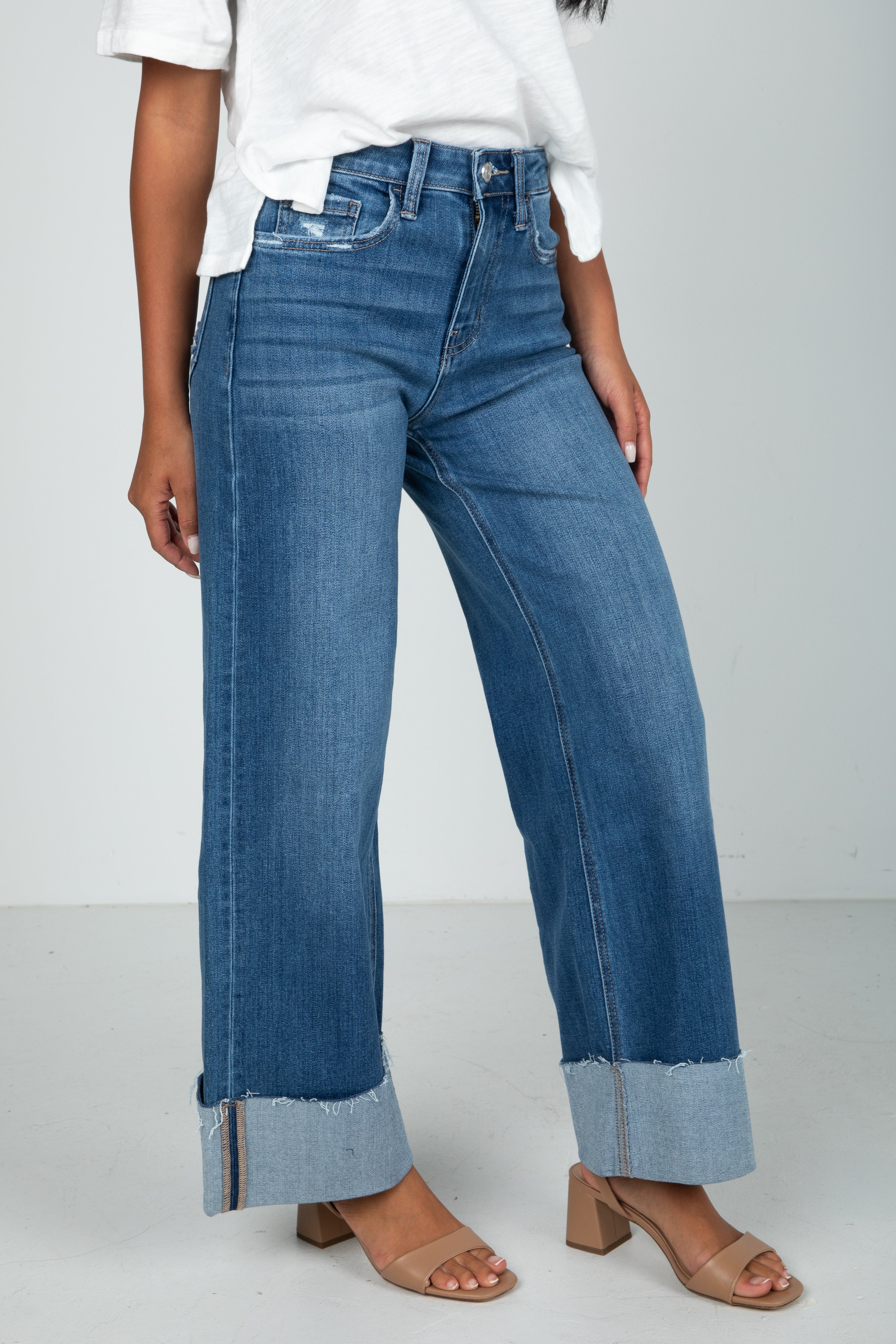 Person wearing blue jeans with a white shirt on a plain background