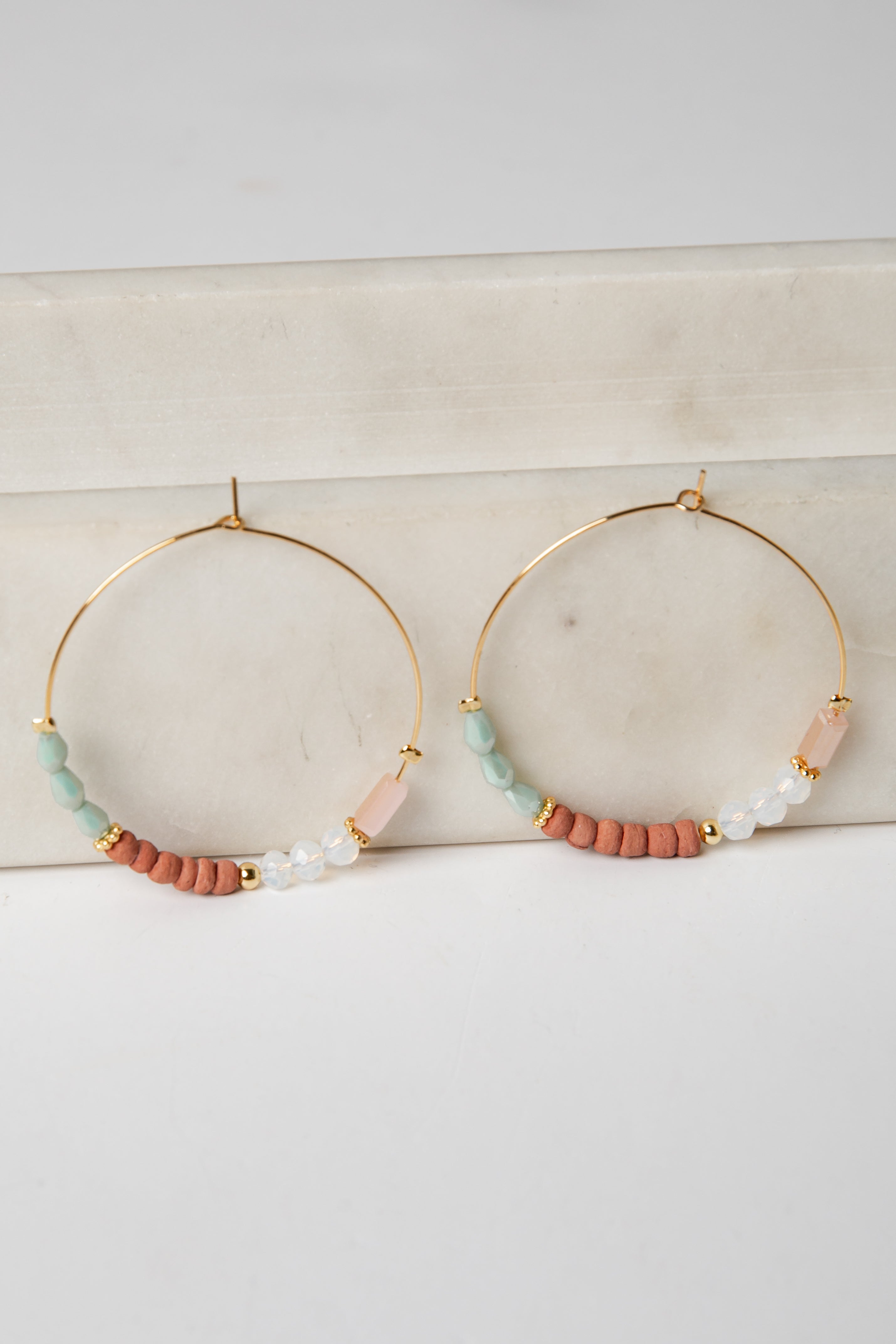 Gold hoop earrings with colorful beads on a light surface