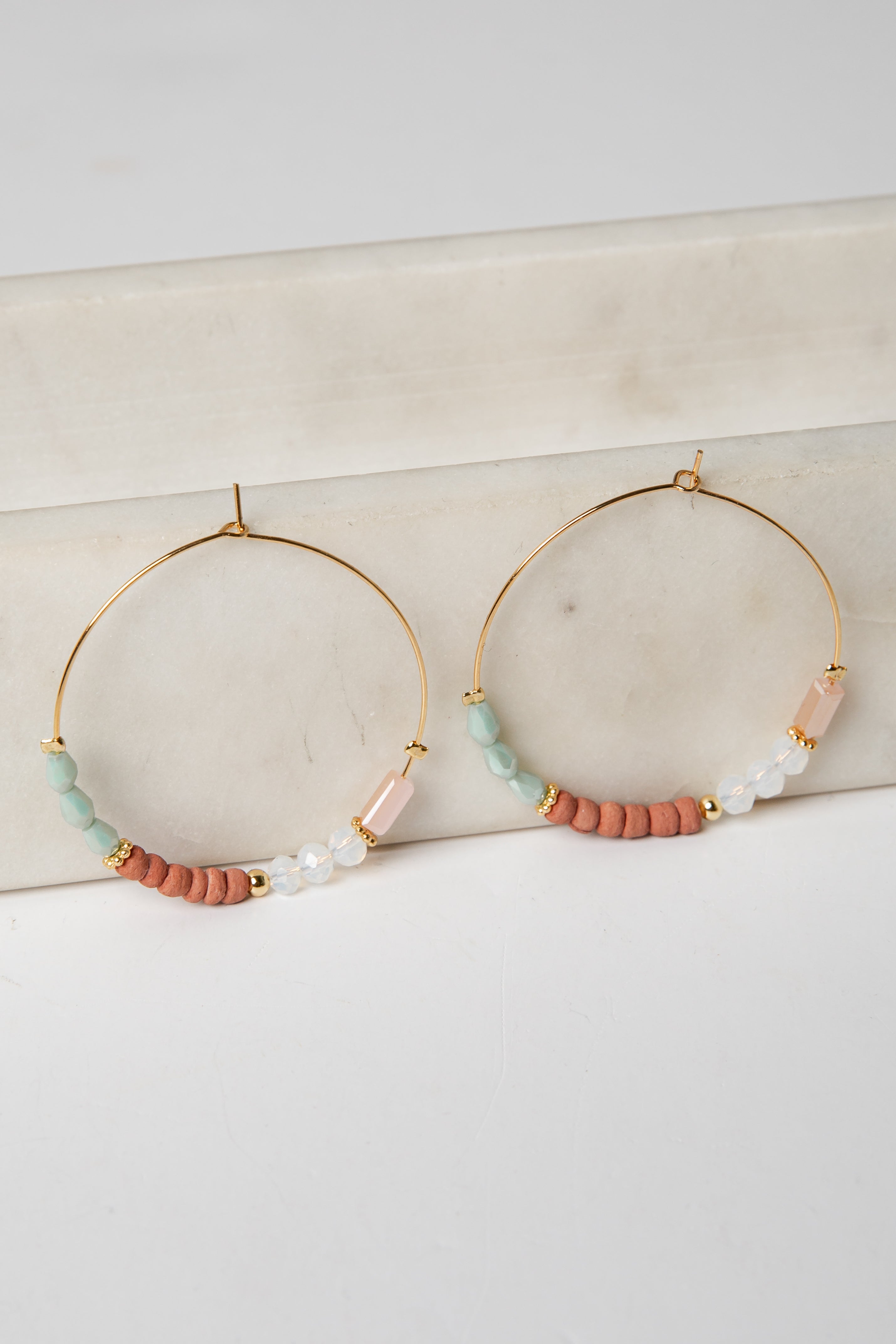 Gold hoop earrings with colorful beads on a marble surface