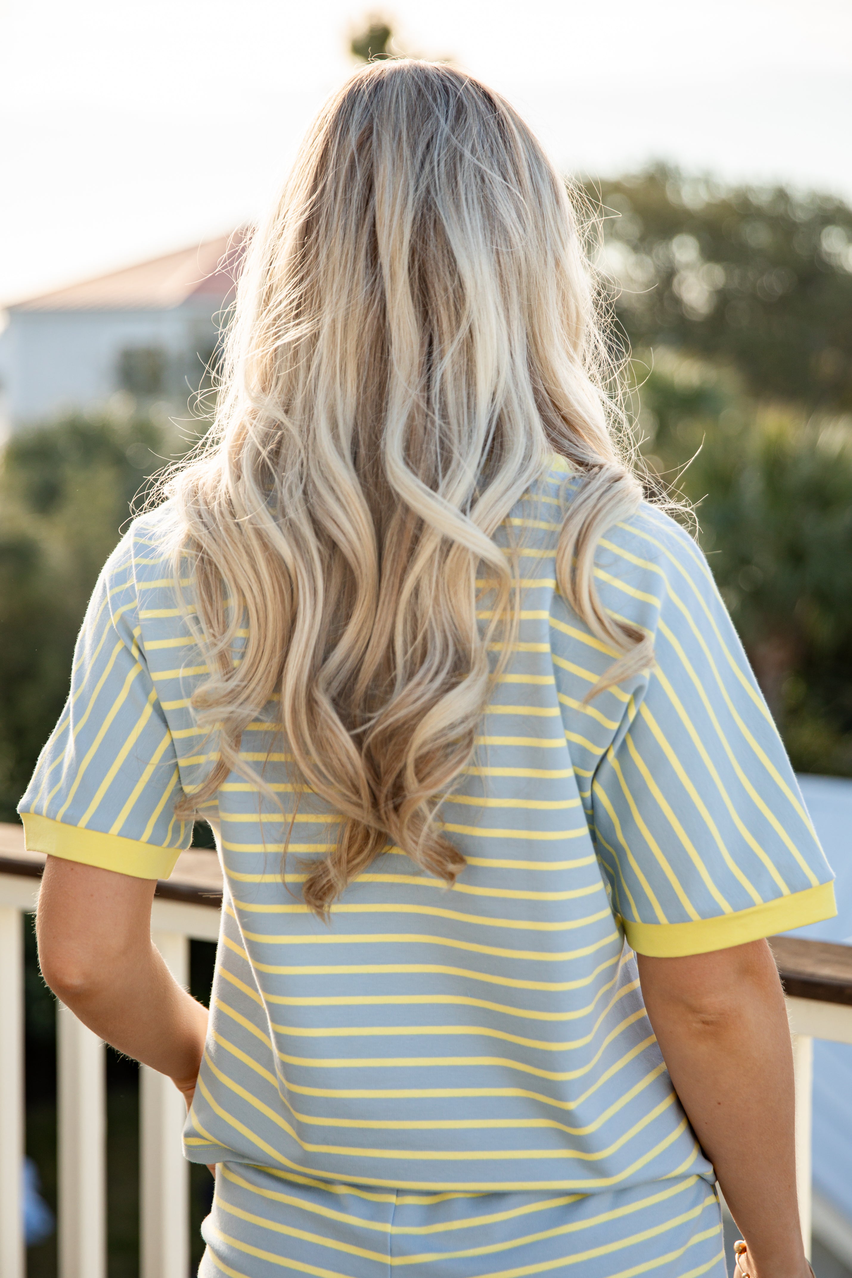 Person wearing a yellow and blue striped shirt with long blonde hair, standing outdoors.
