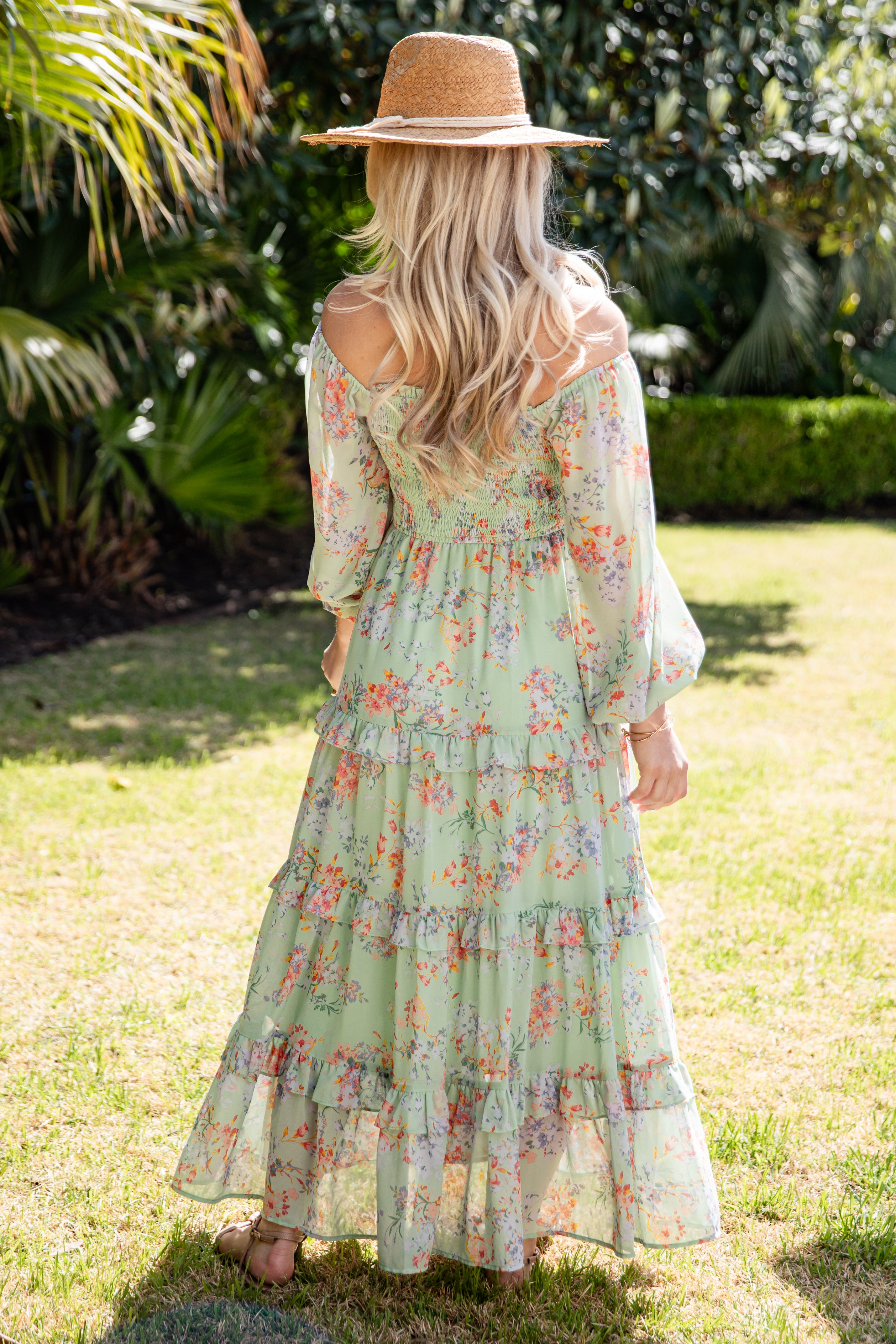 Woman in a floral dress and straw hat standing in a garden