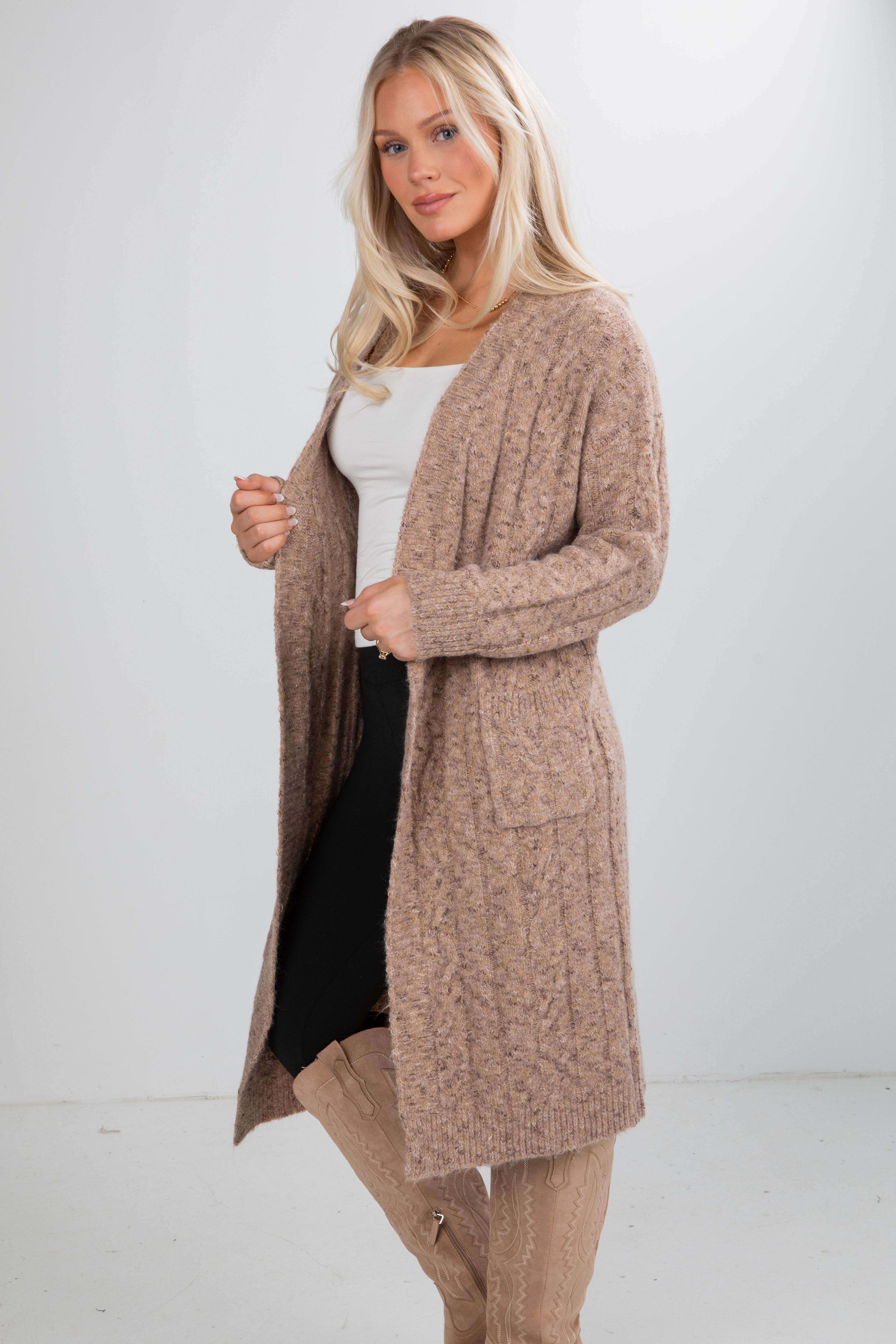 Woman wearing a long beige cardigan over a white top and black skirt on a white background