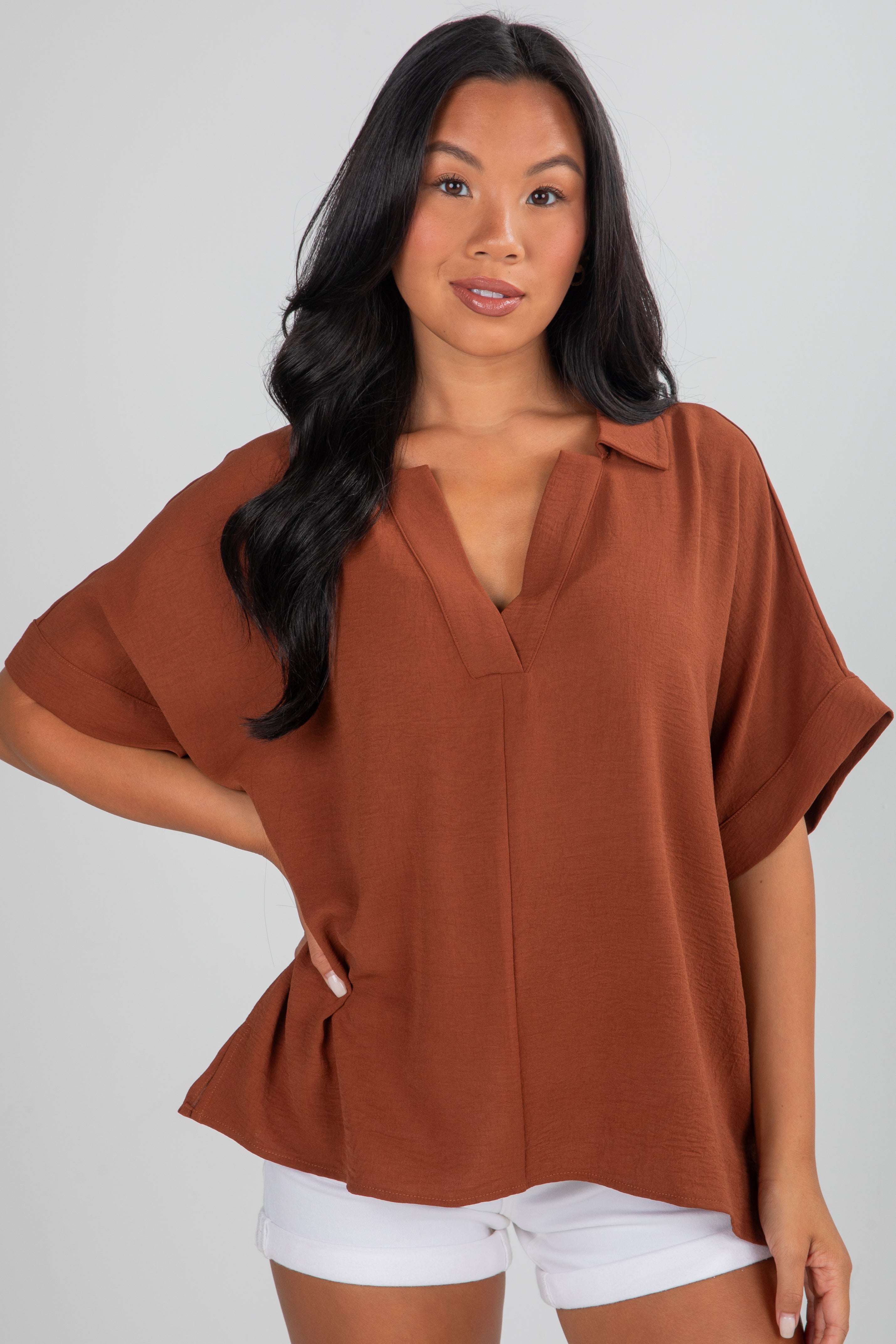 Woman wearing a brown top and white shorts on a plain background