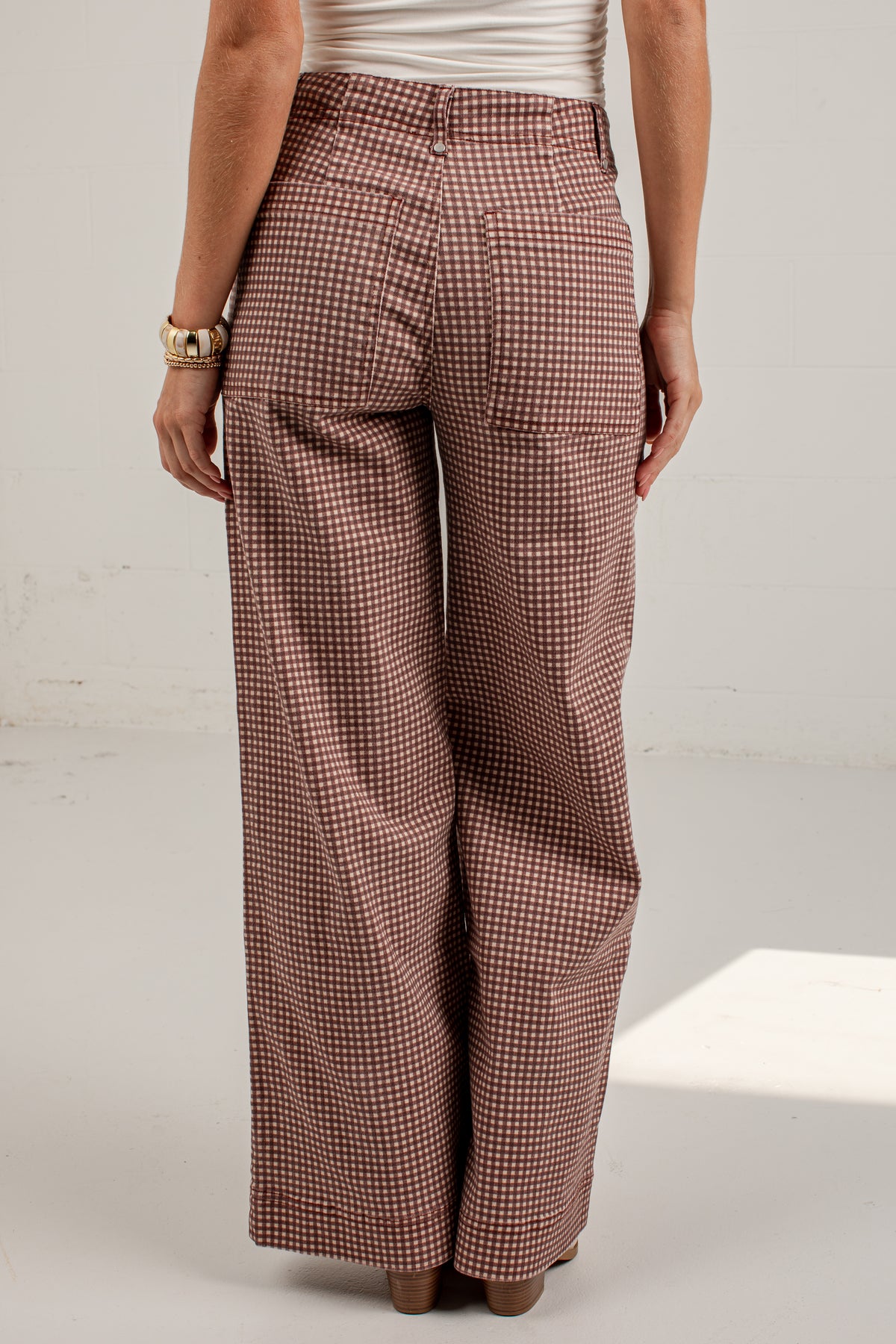 A person shown from the back wearing high-waisted, wide-leg trousers with a small-scale brown and white houndstooth pattern, paired with a white ribbed top and brown heels.
