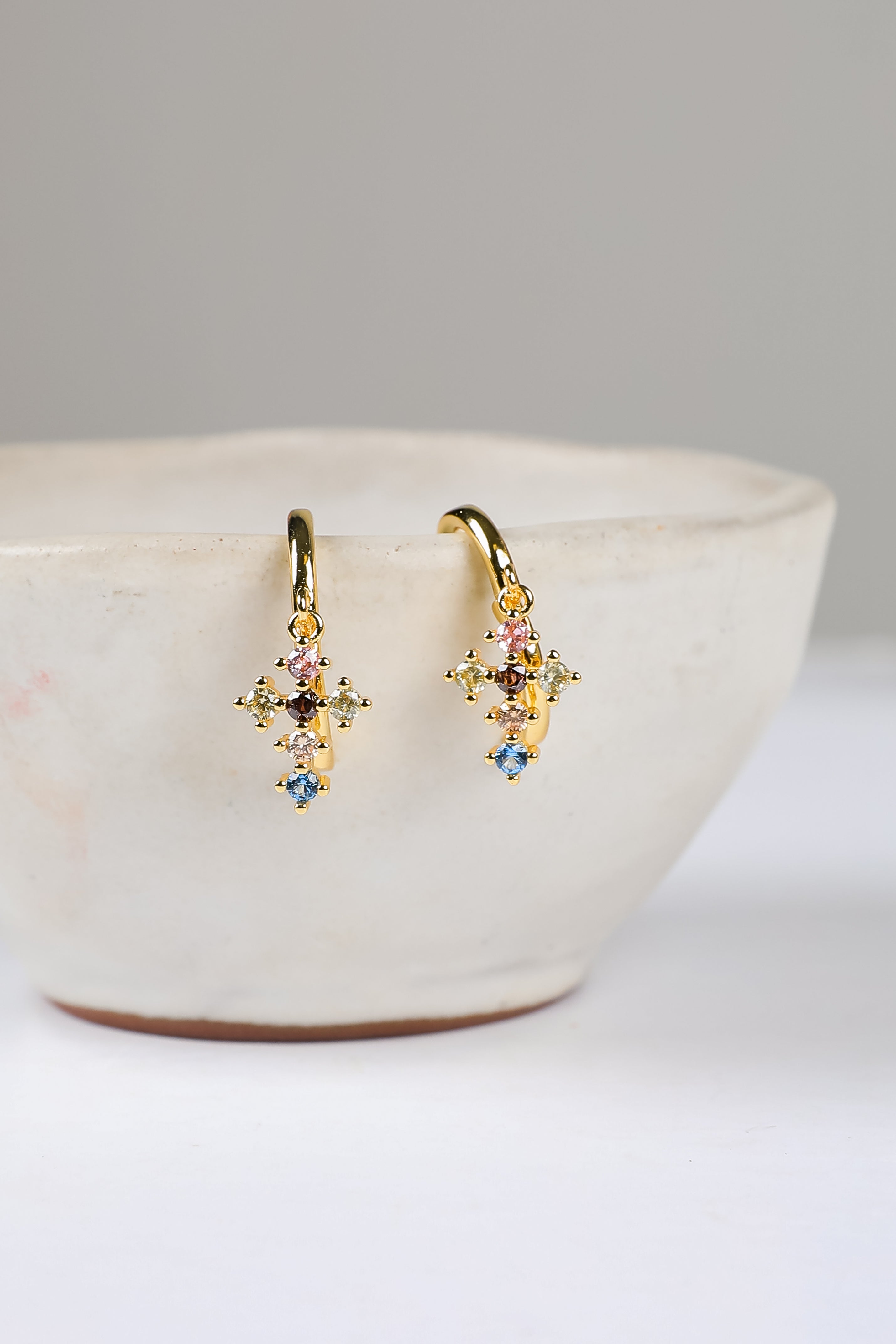 Gold earrings with colorful stones on a white bowl