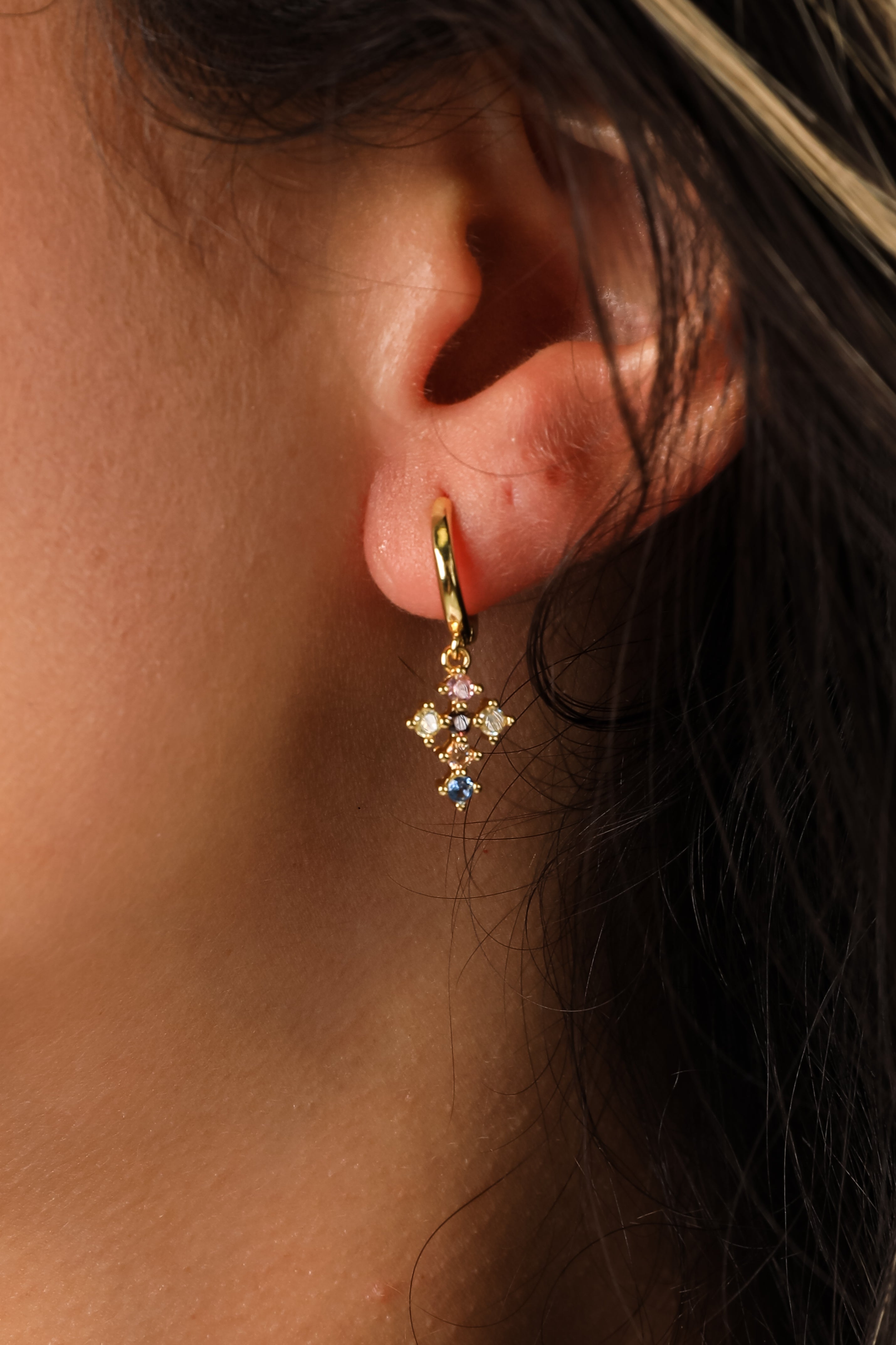 Close-up of an ear wearing a gold earring with gemstones.