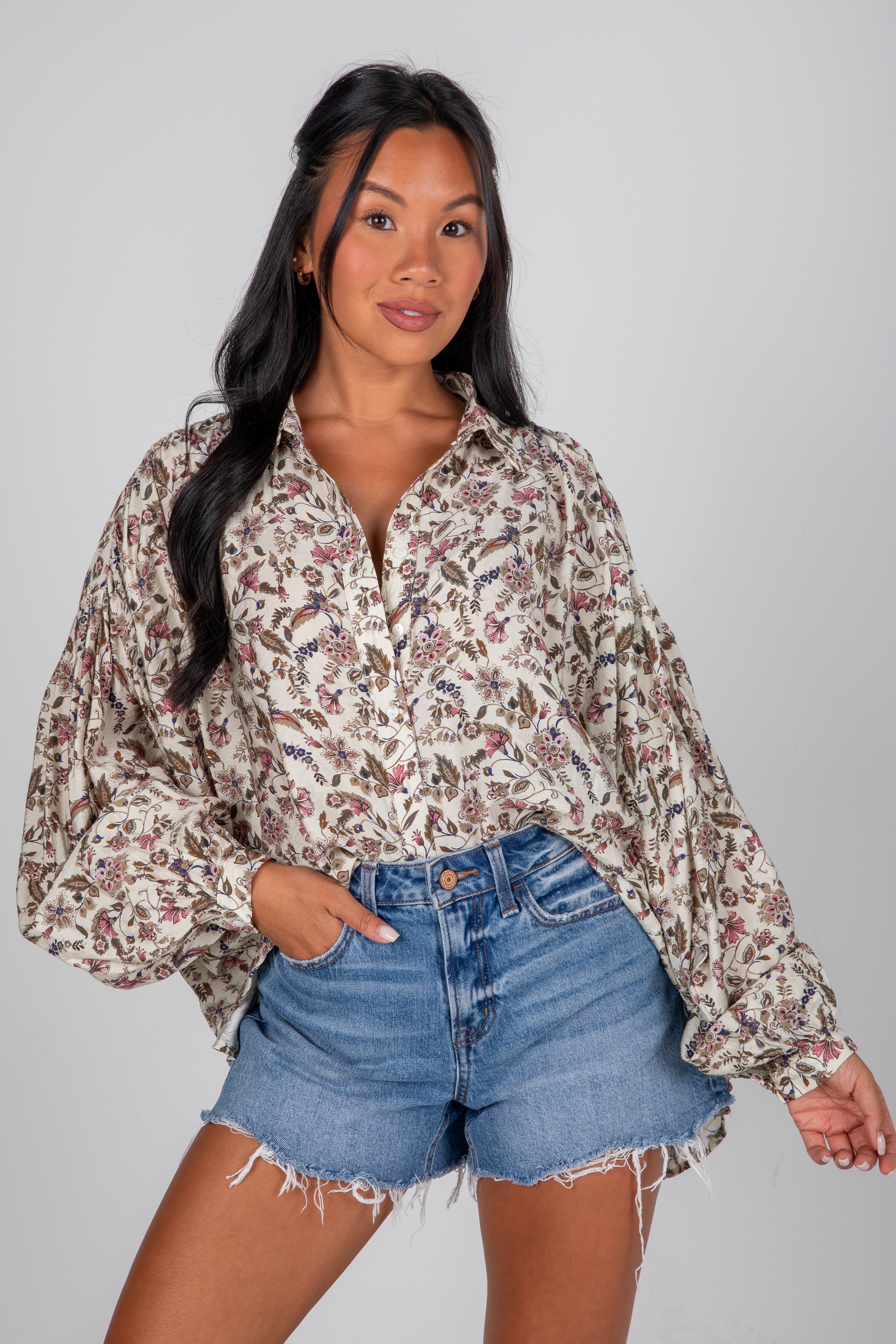 Woman wearing a floral blouse and denim shorts on a plain background