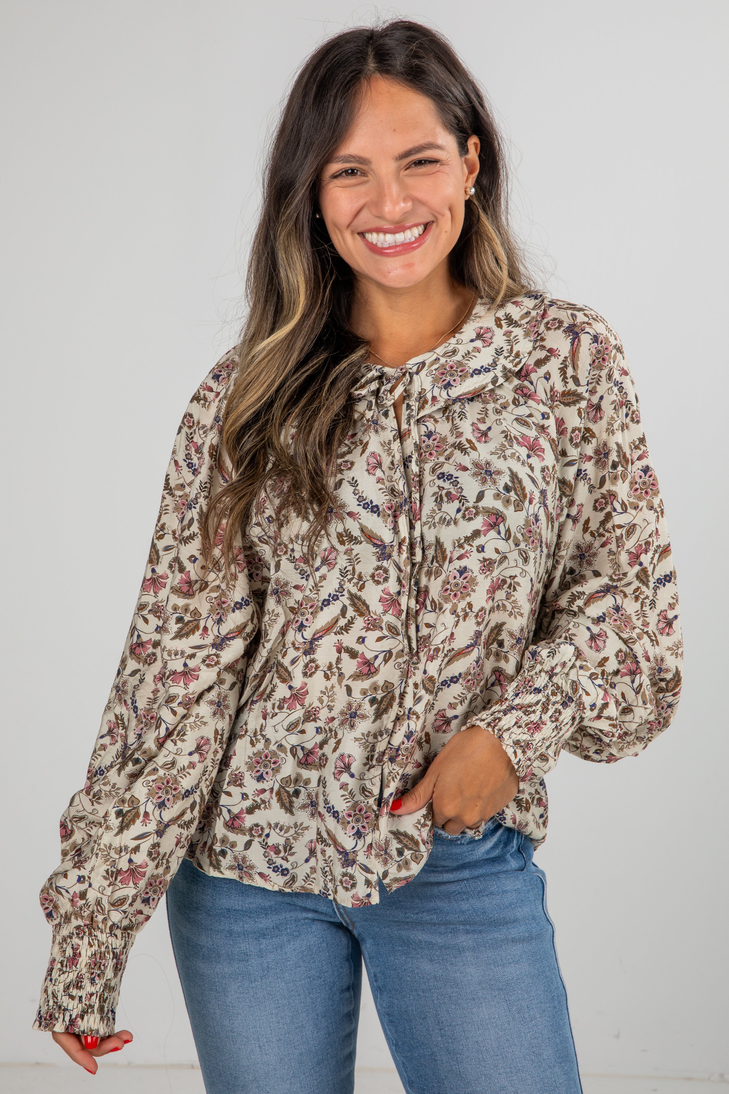 Woman wearing a floral blouse and blue jeans against a plain background