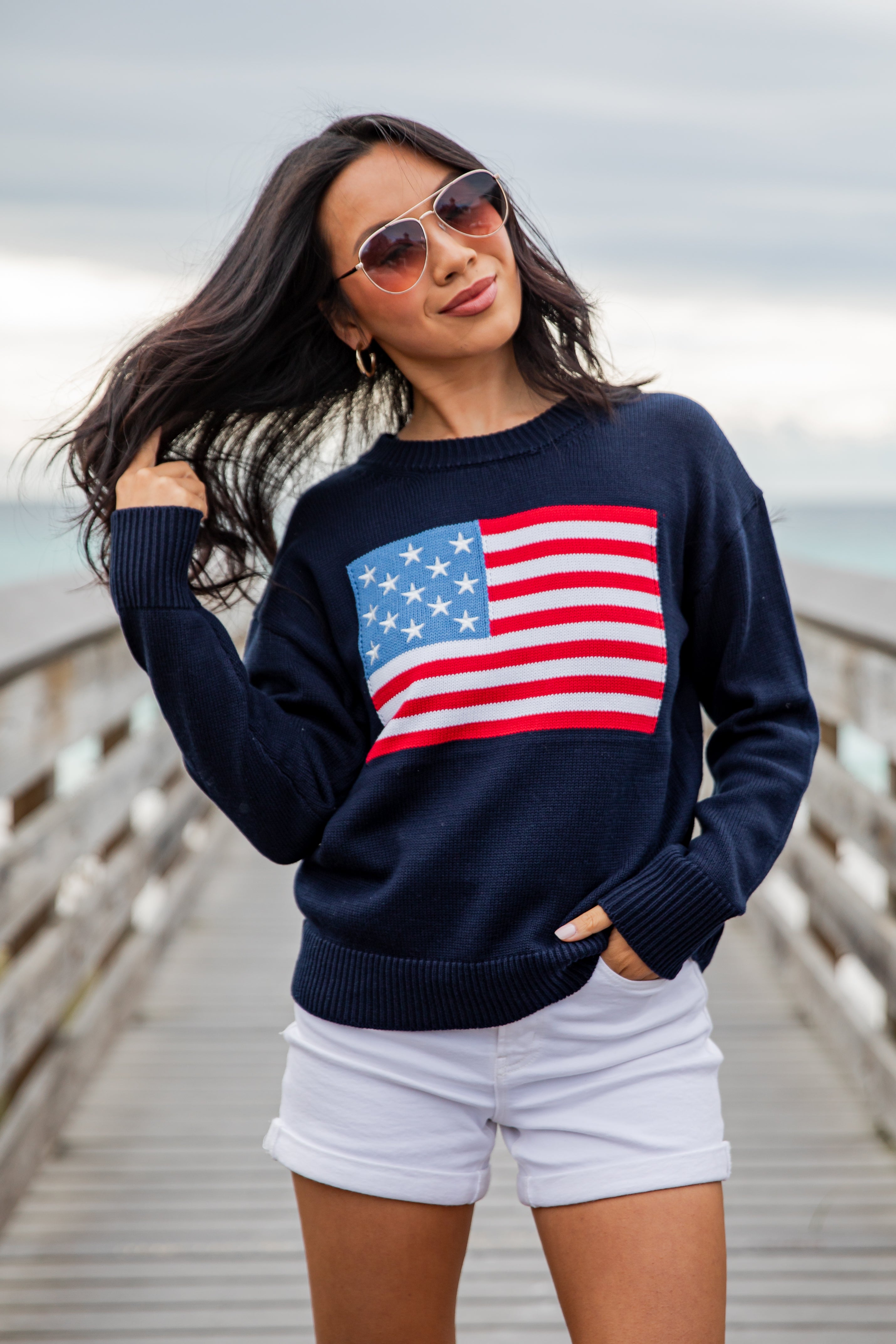 Woman wearing a navy sweater with an American flag design on a wooden pier.