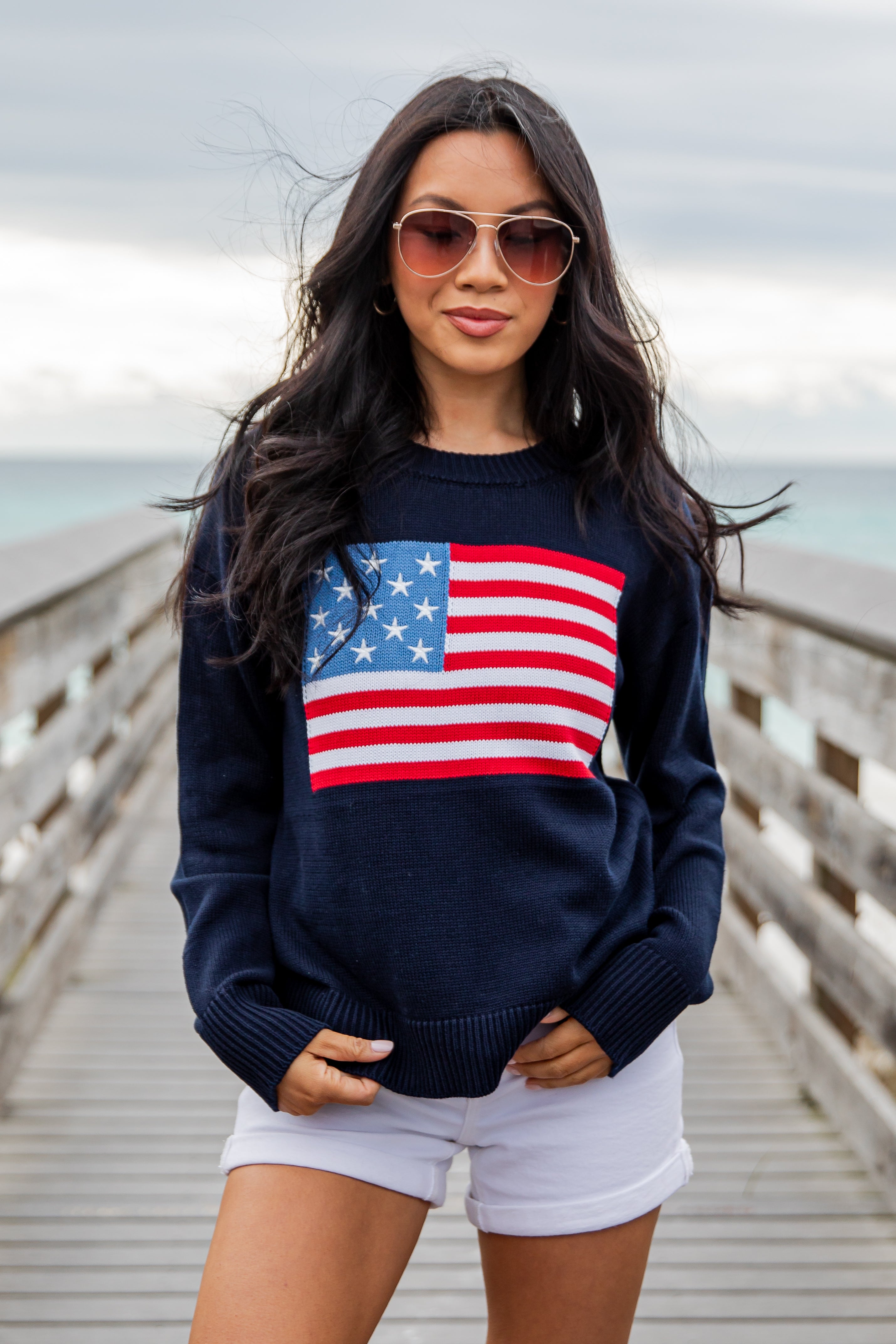 Woman wearing a navy blue sweater with an American flag design on a wooden pier.