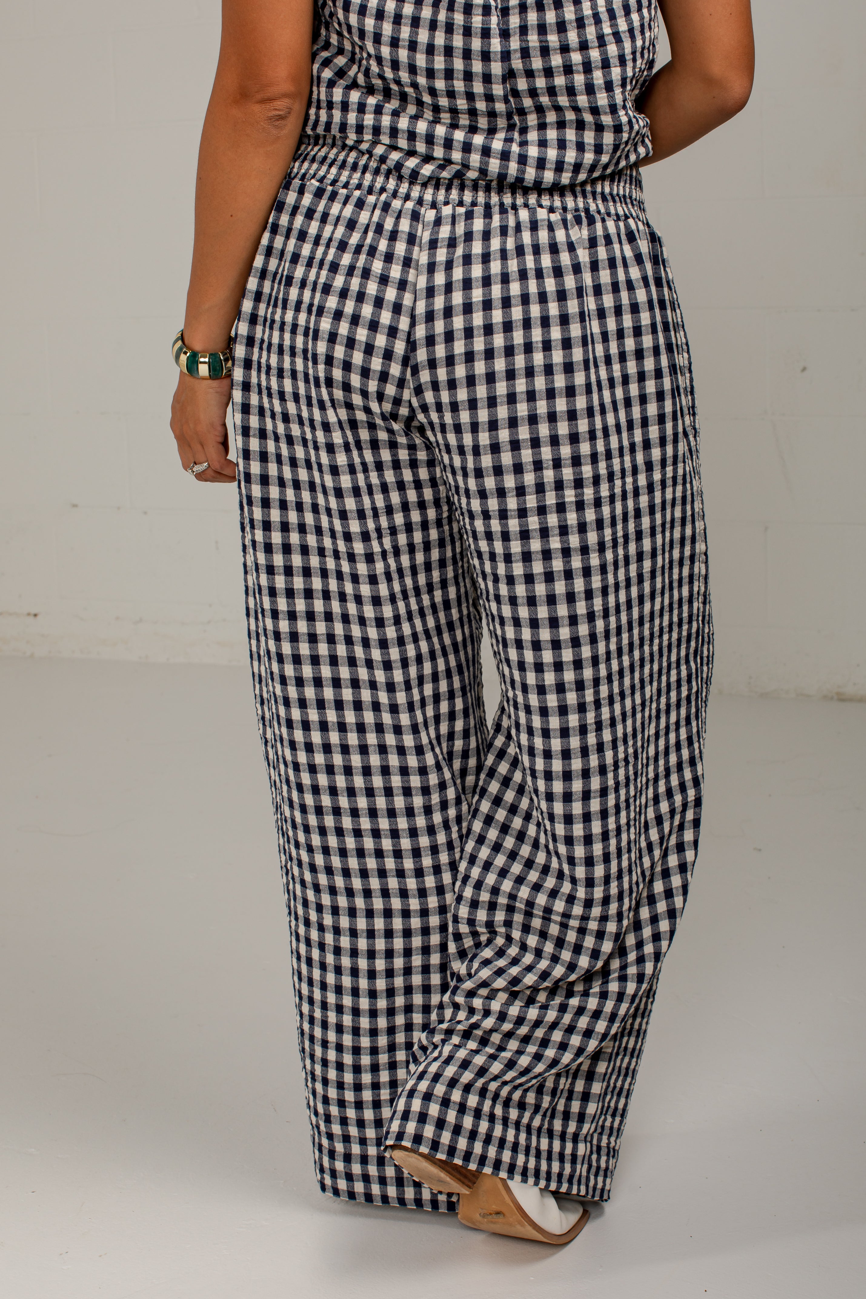 A person wearing loose, wide-leg pants with a navy and white gingham check pattern, shown from the back against a plain light gray studio background.