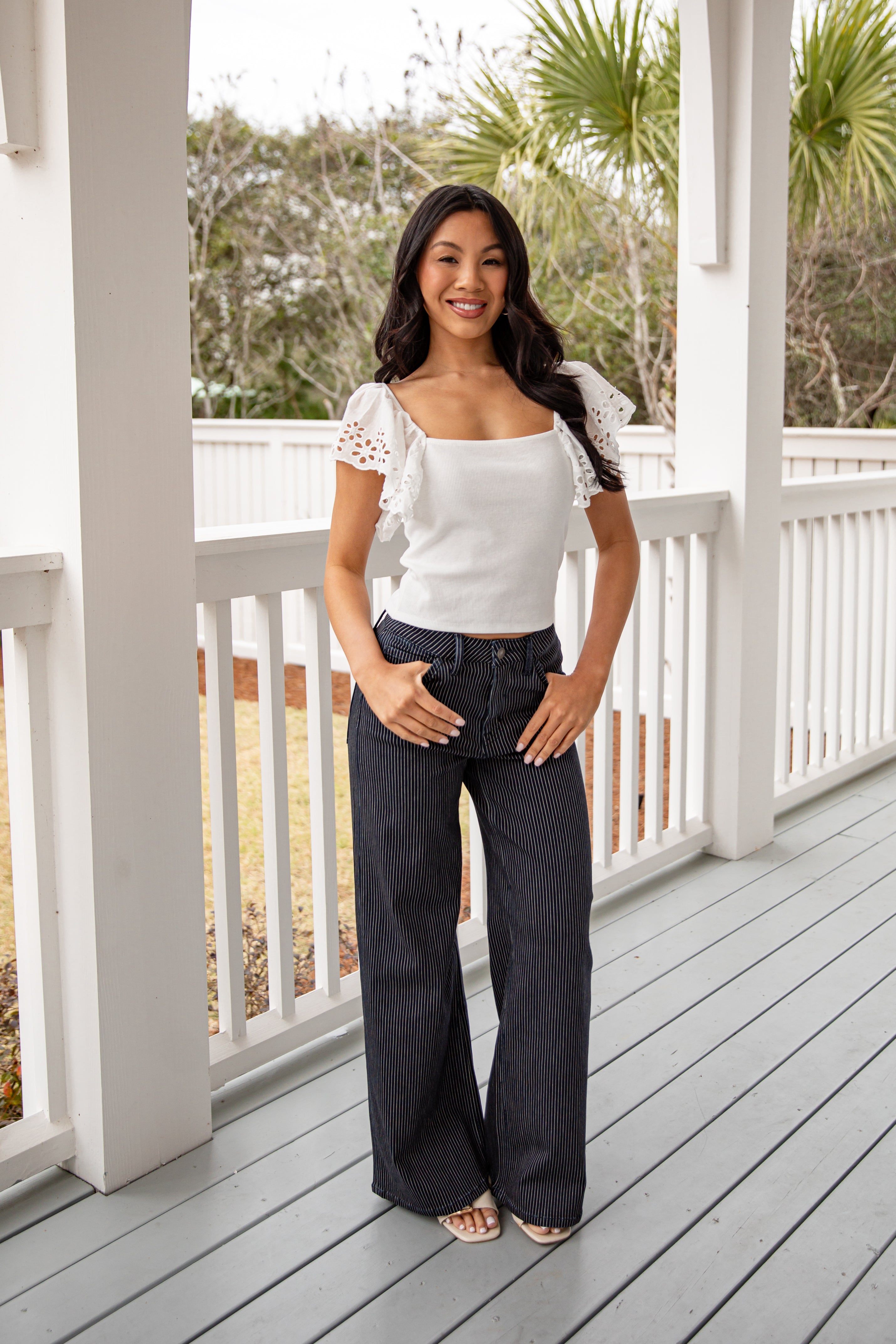Woman standing on a porch wearing a white top and dark jeans.