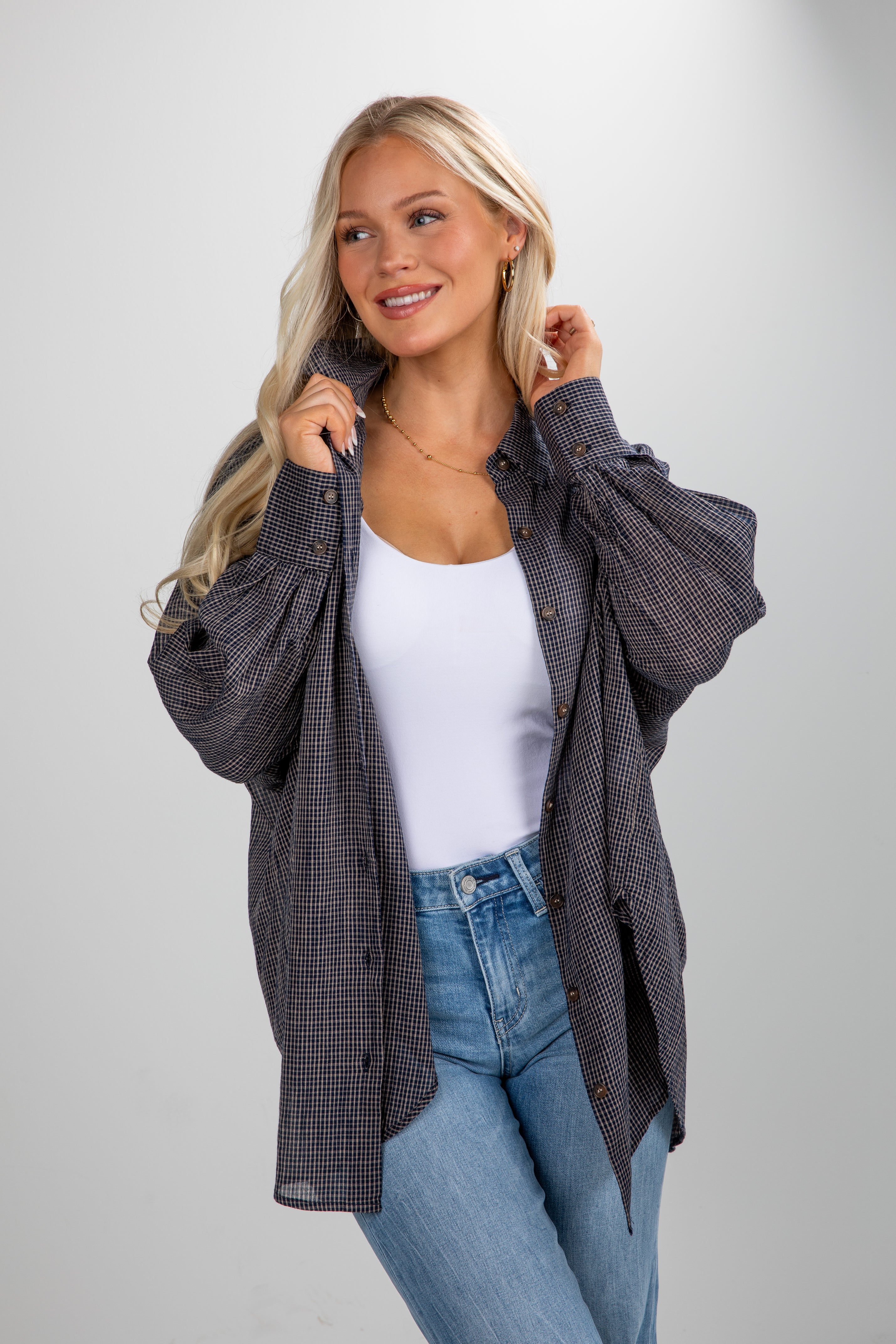 Woman wearing a plaid shirt over a white top and blue jeans on a gray background
