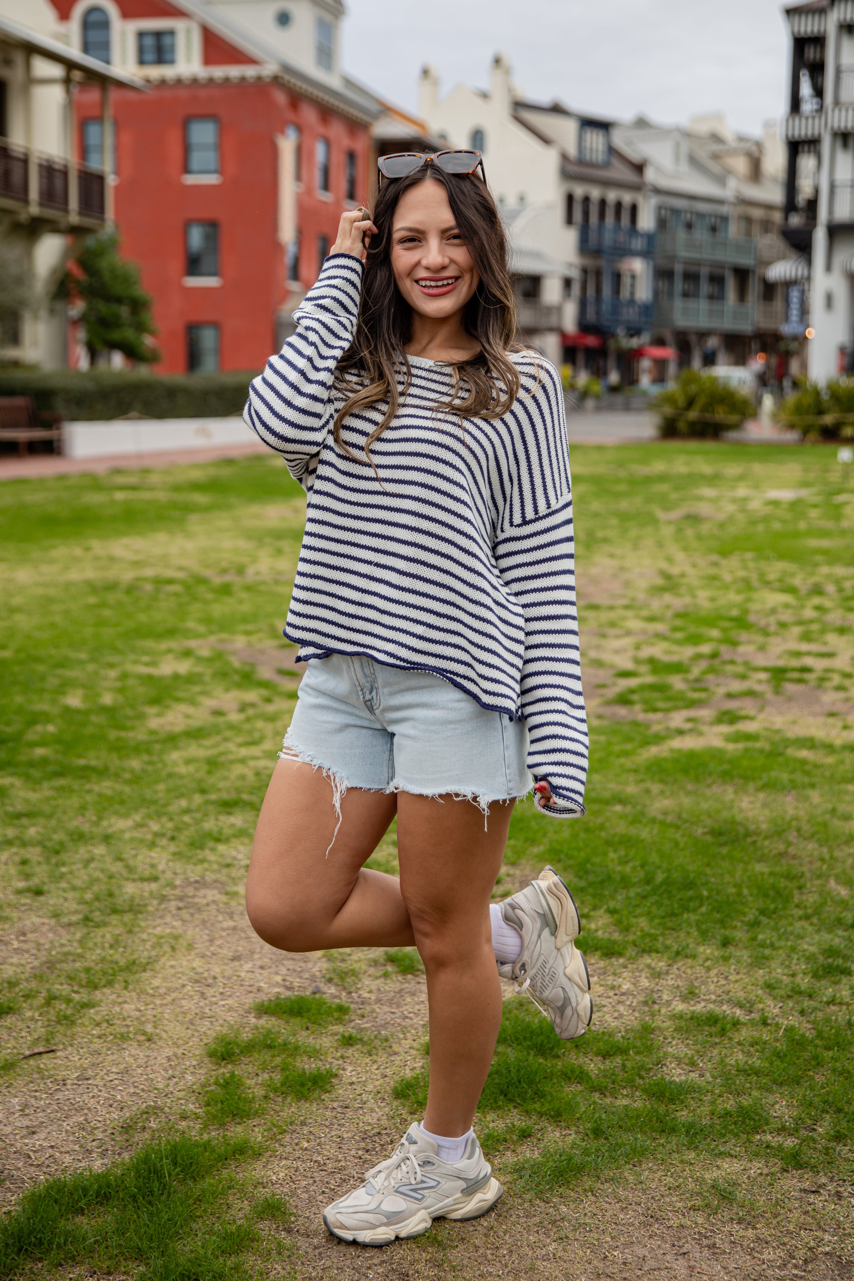 Woman in a striped sweater and denim shorts posing outdoors.